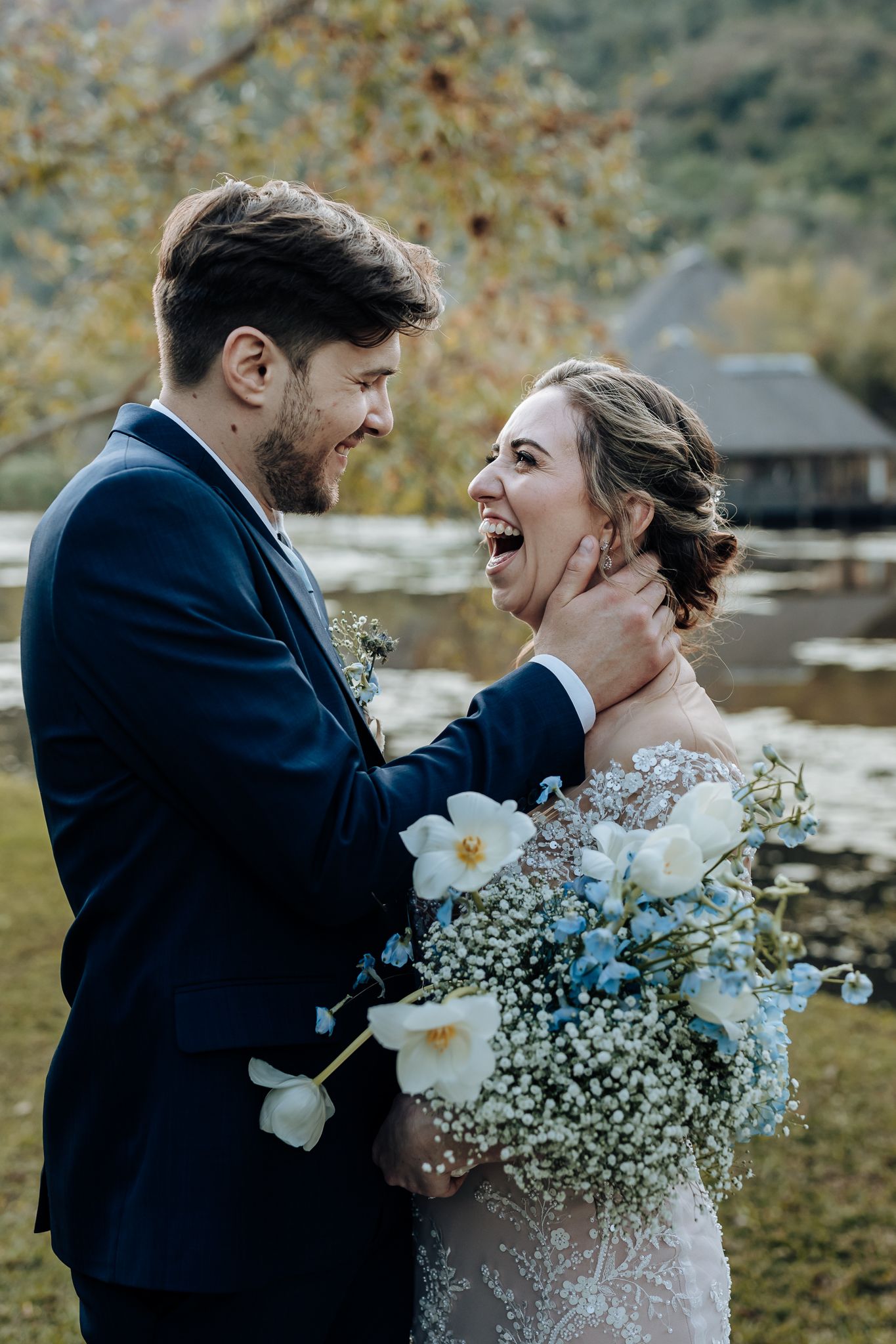 Joyful wedding moment with laughter and white flowers against an autumn lakeside landscape.