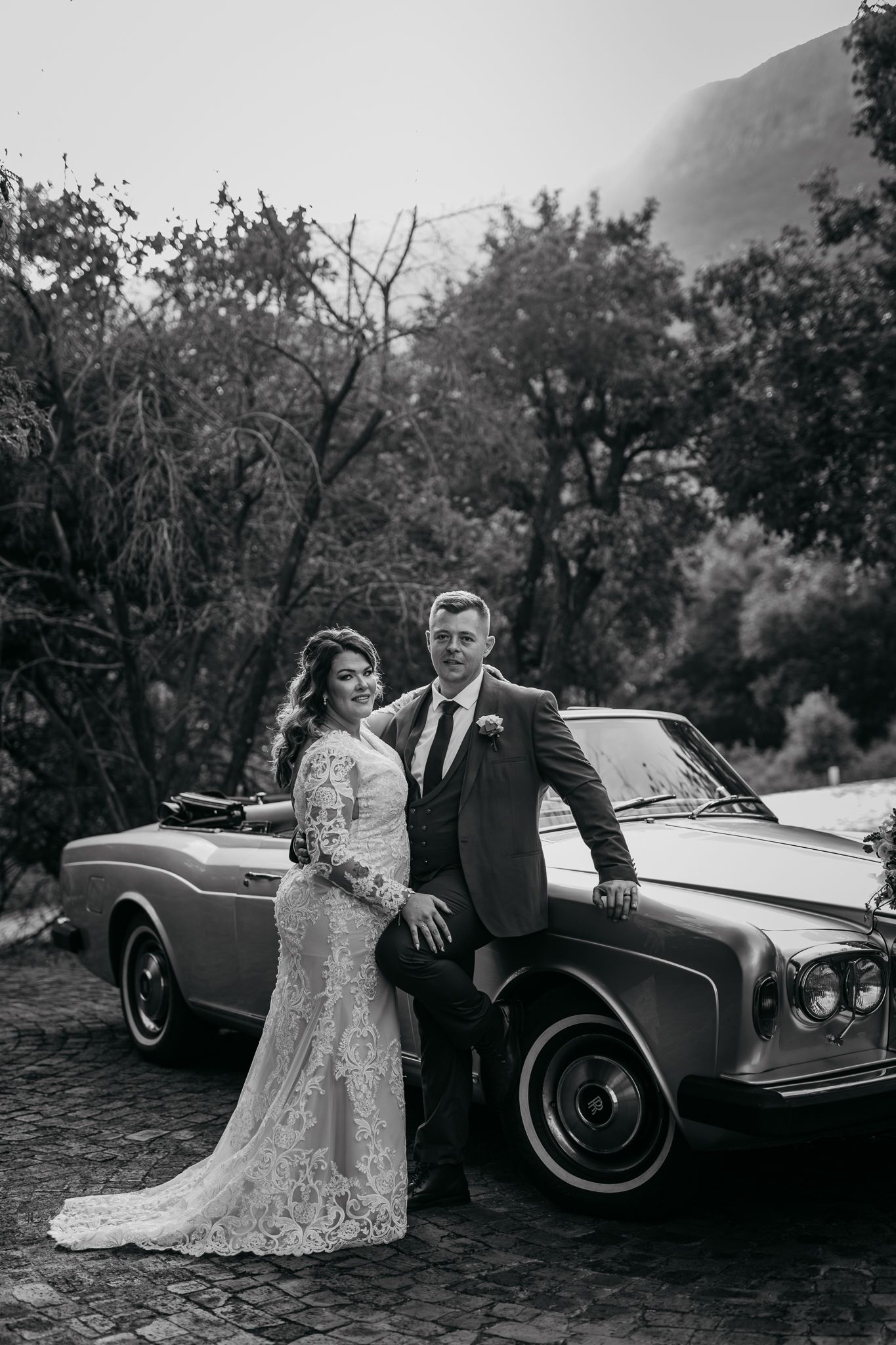 Black and white portrait of newlyweds posing with classic Rolls Royce convertible.
