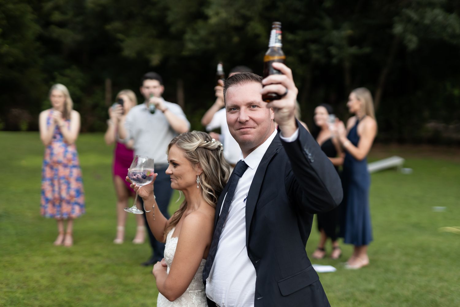 Wedding celebration on a grassy lawn with guests enjoying drinks outdoors.