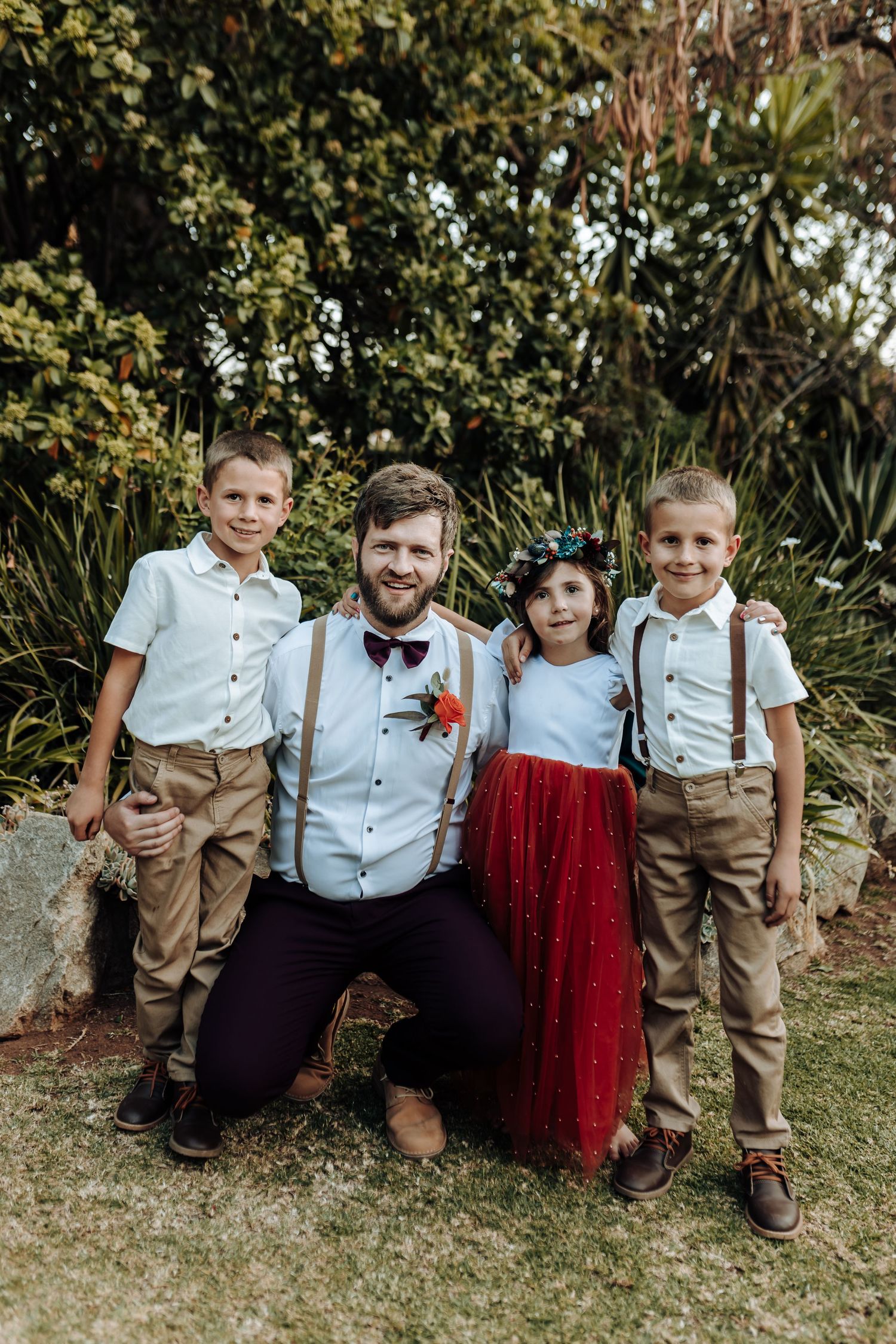 Wedding party portrait with children in coordinated attire against garden setting.