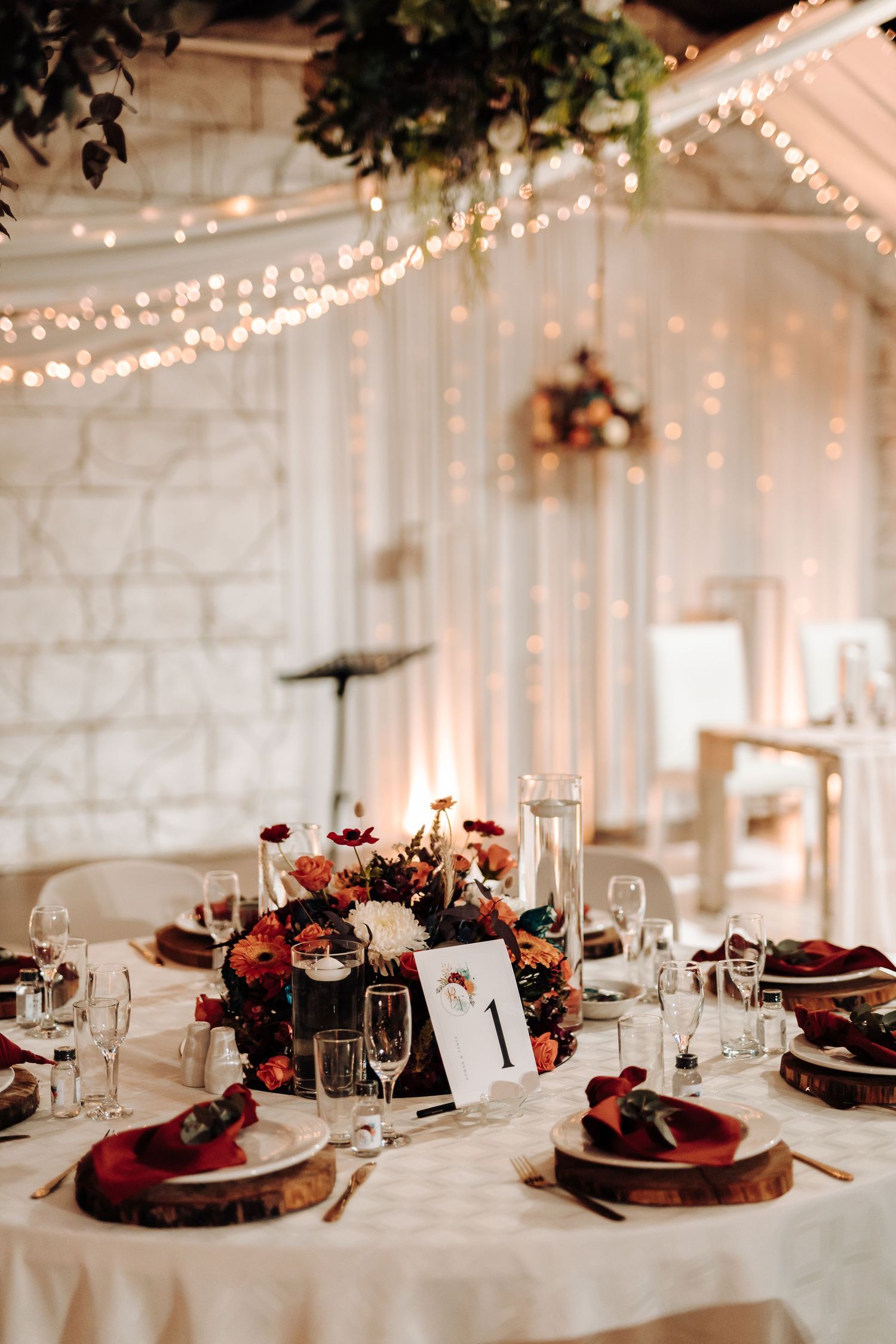 Romantic wedding table setting with floral centerpiece, string lights, and white stone wall backdrop.