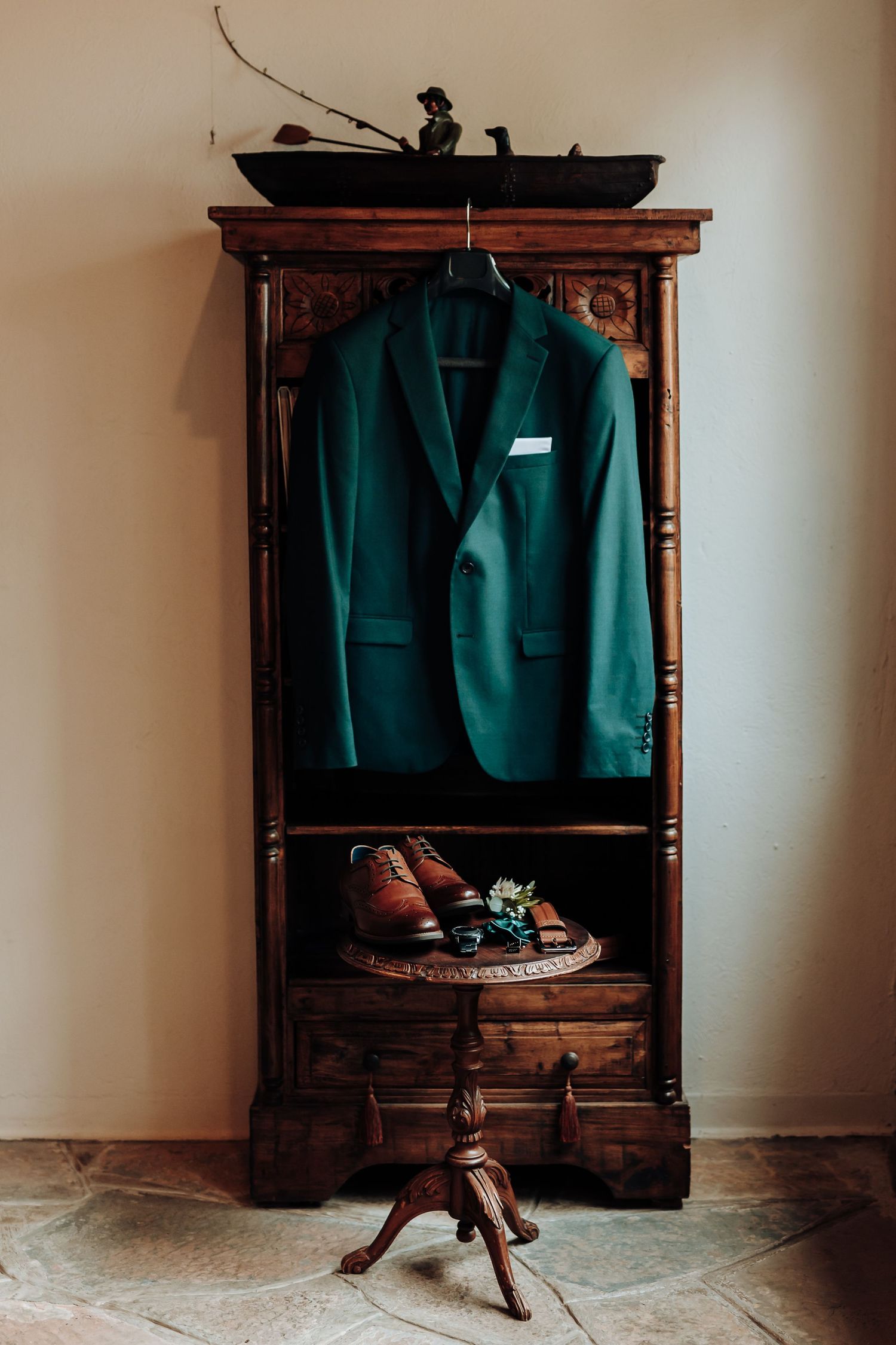 Vintage wooden armoire displaying an elegant emerald green suit jacket and brown leather shoes on a rustic stand.