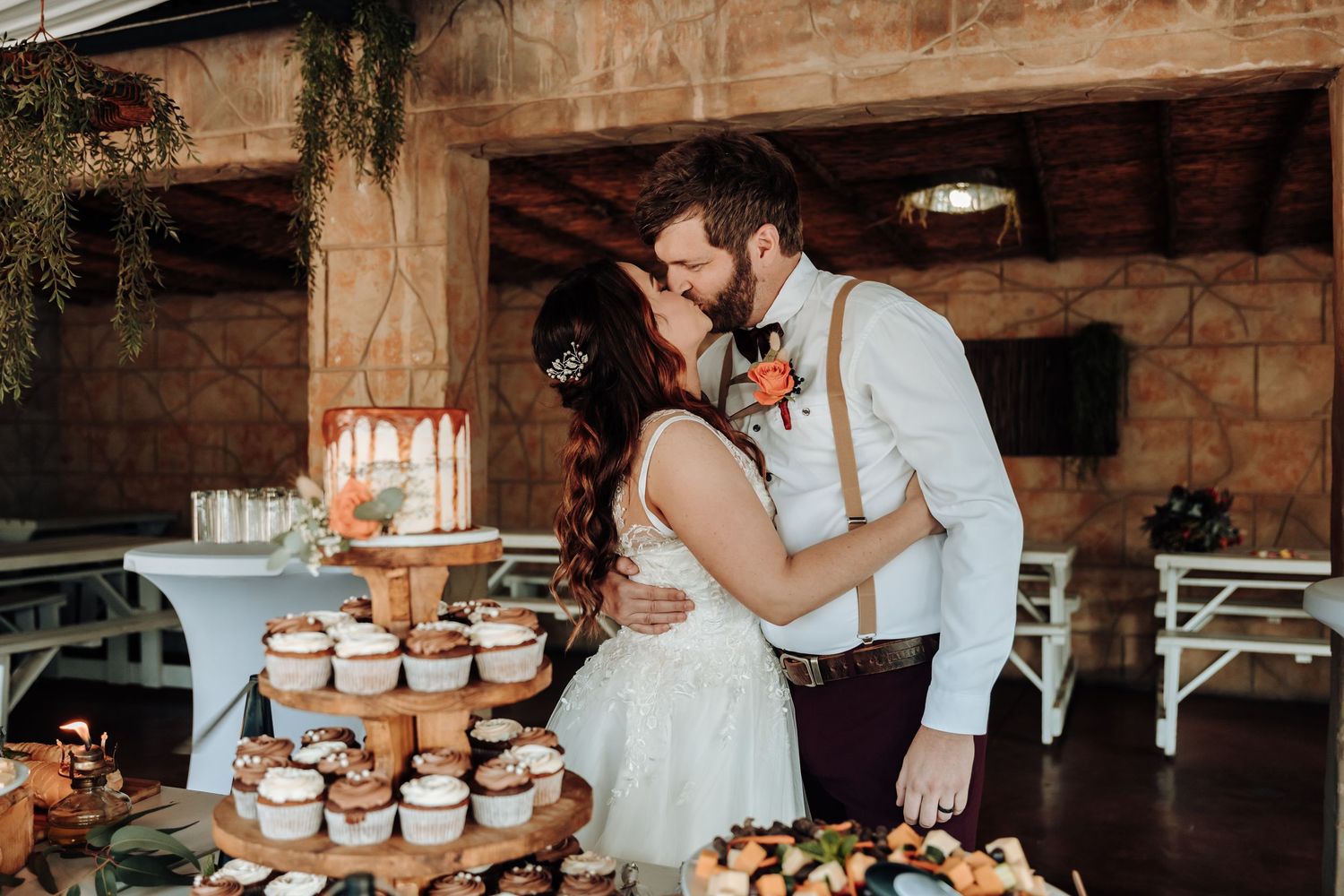 Couple sharing intimate moment by multi-tiered cupcake display at rustic venue.