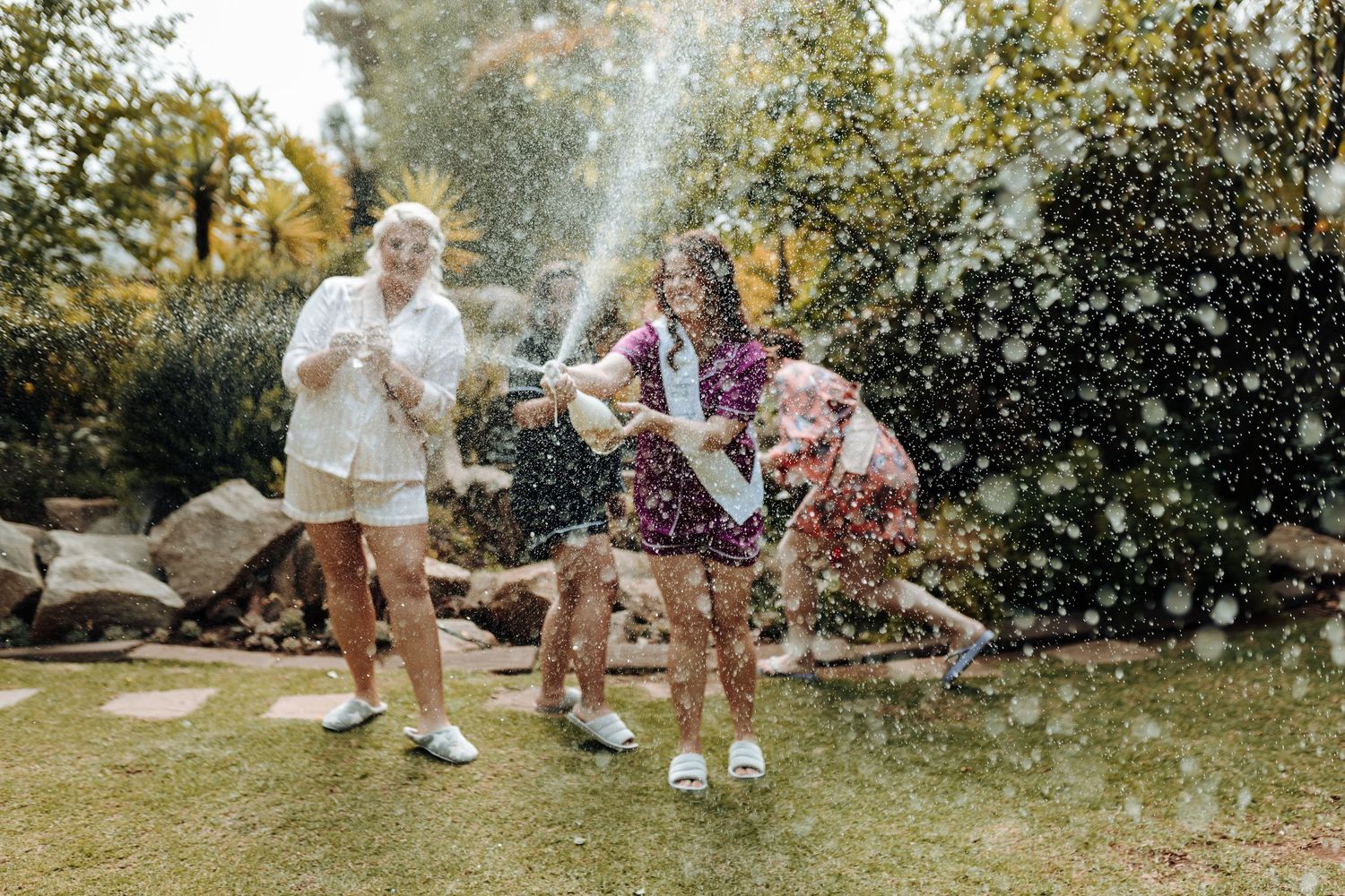 Joyful celebration with champagne spraying in an outdoor garden setting.