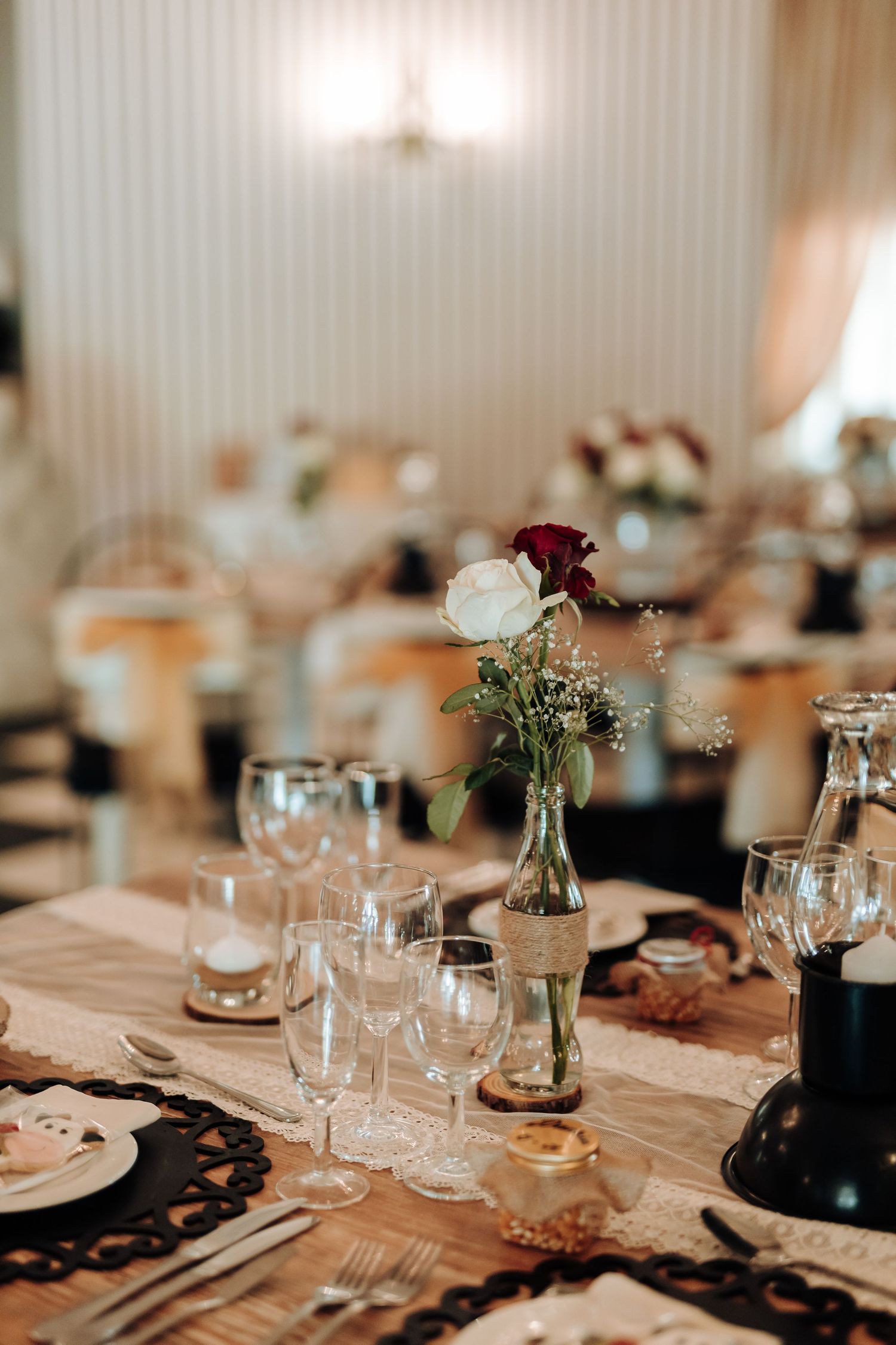Elegant wedding reception table with wine glasses and delicate floral centerpiece featuring red and white roses.