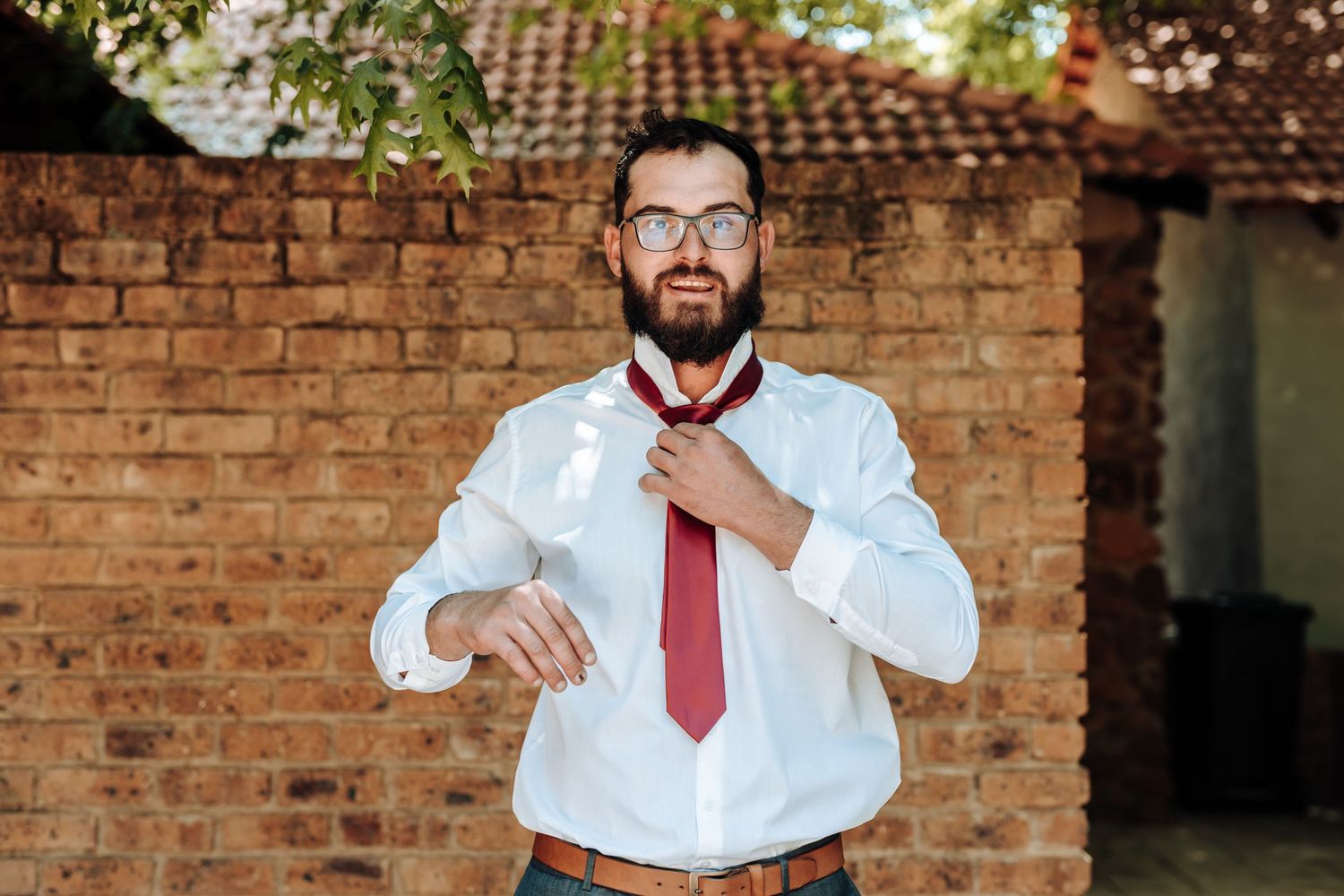 Professional adjusting red tie while standing against brick wall backdrop.
