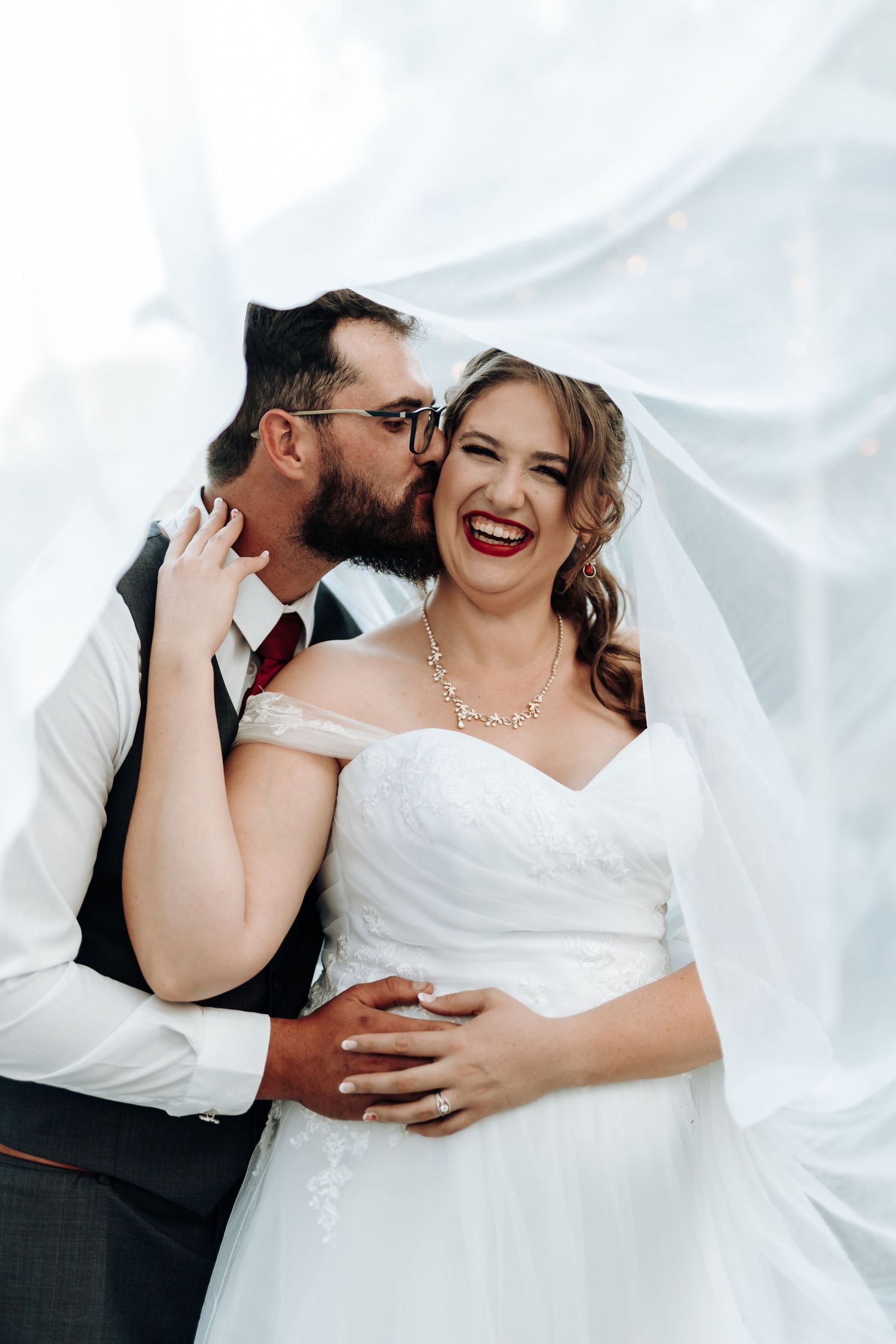 Joyful wedding moment captured against white fabric backdrop.