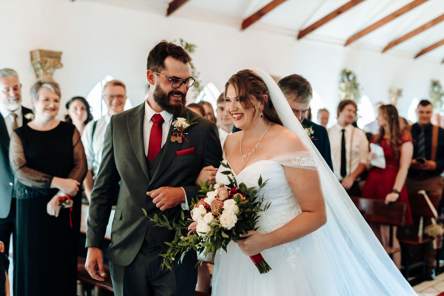 A joyful wedding ceremony moment inside a chapel with white walls and exposed wooden beams.