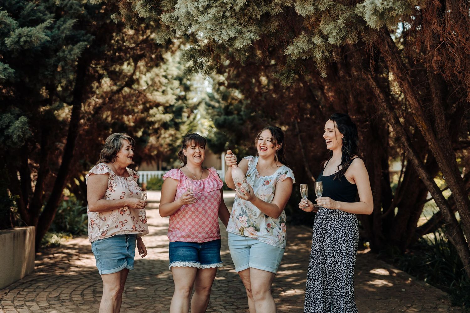 Friends walking together holding drinks in a tree-lined outdoor path.