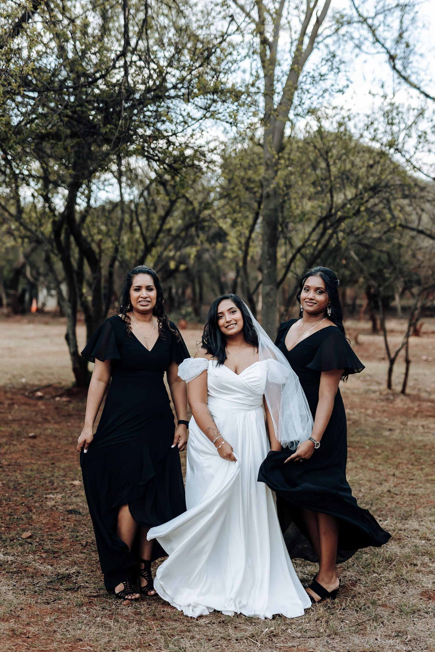 Three women in black and white dresses pose together in a natural outdoor setting.
