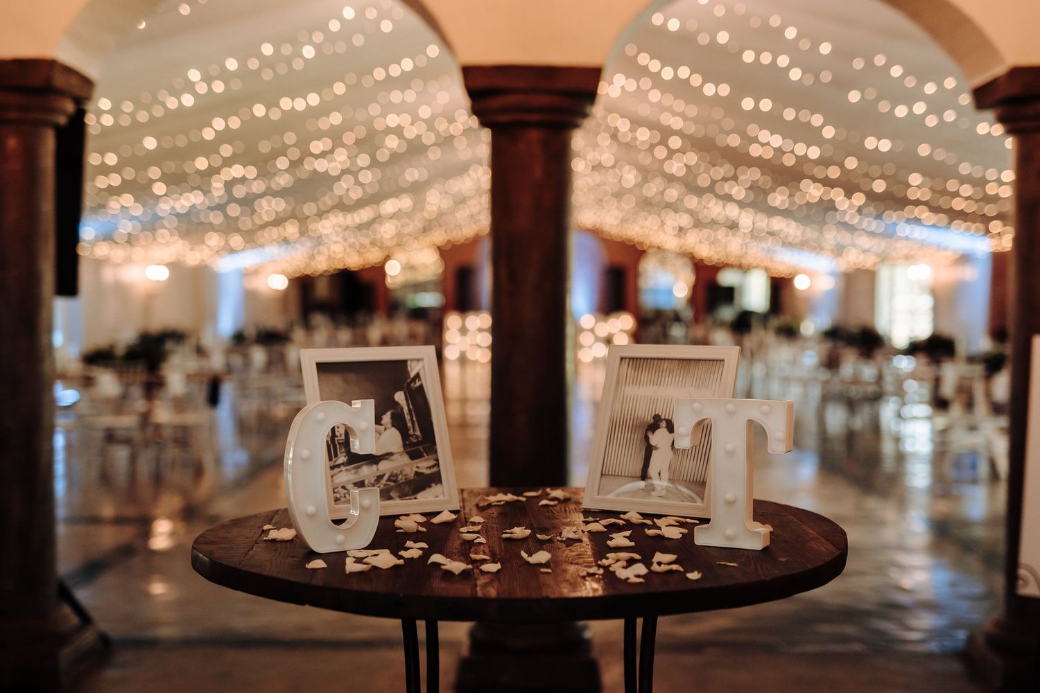 Vintage photographs and decorative elements displayed on a table under twinkling string lights at a wedding reception.