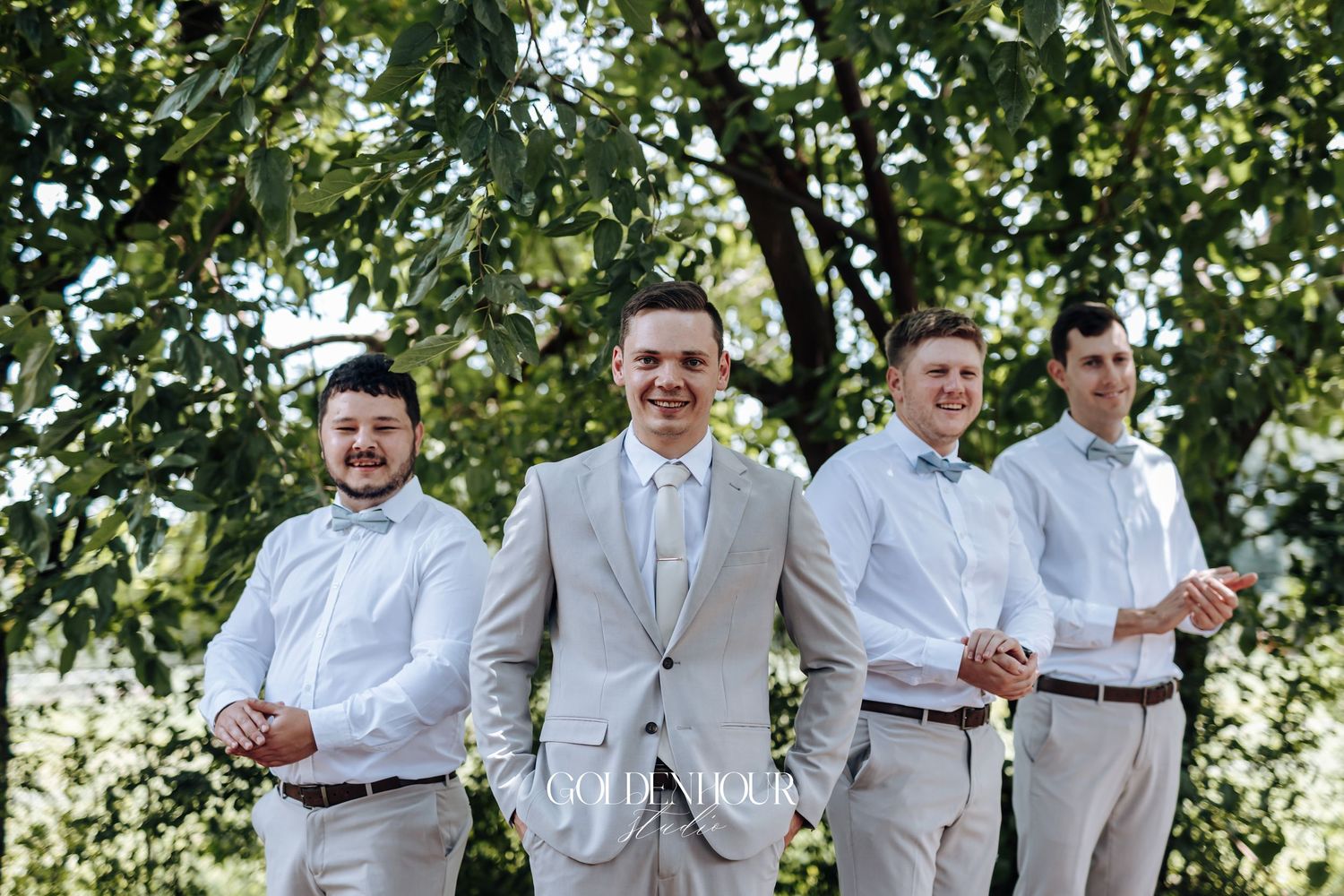 Wedding party wearing coordinated white shirts and brown belts pose outdoors.