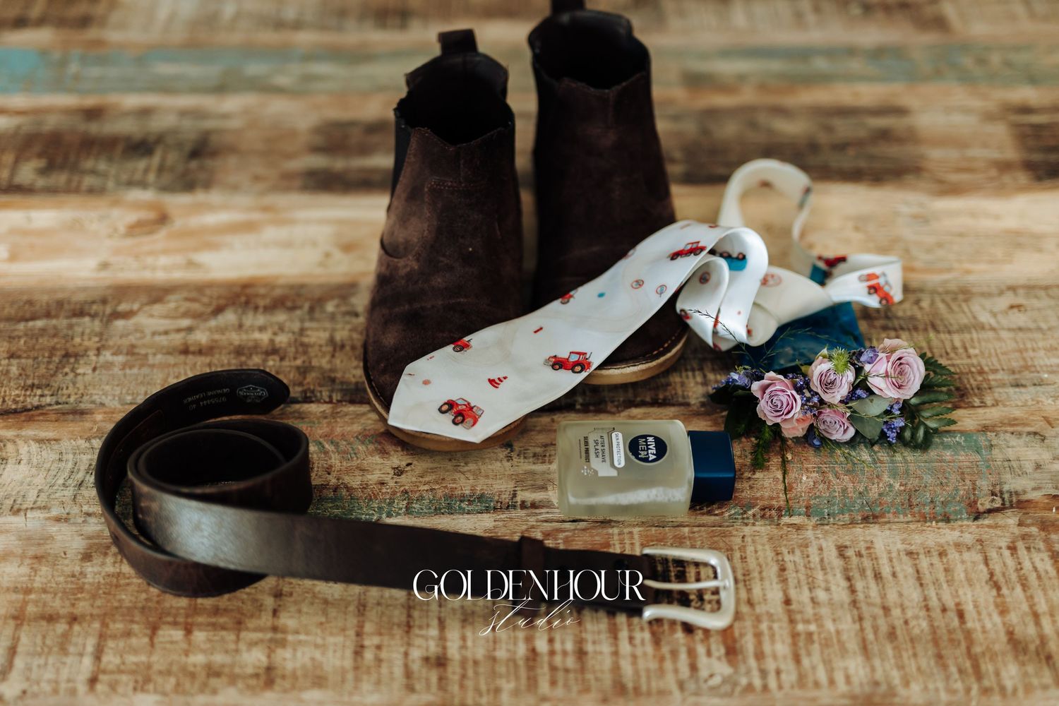 Black dress shoes and accessories arranged on rustic wooden flooring with delicate floral details.