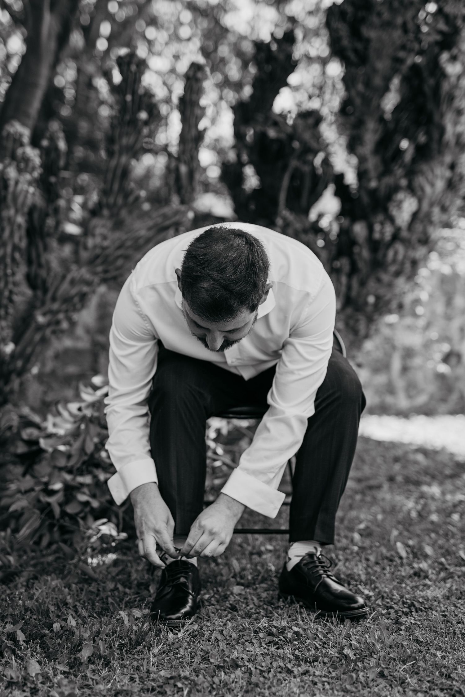 Black and white photo of someone in a white shirt crouching down in a garden setting.