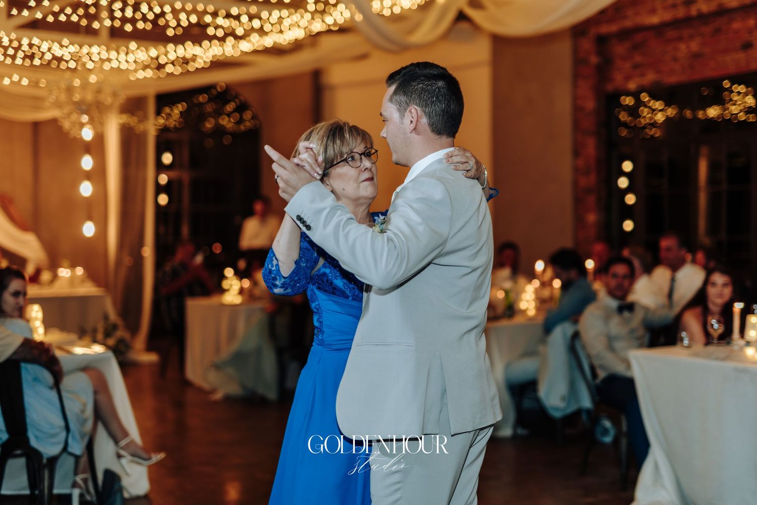 Couples dancing together at a wedding reception under warm string lights and draped fabric.