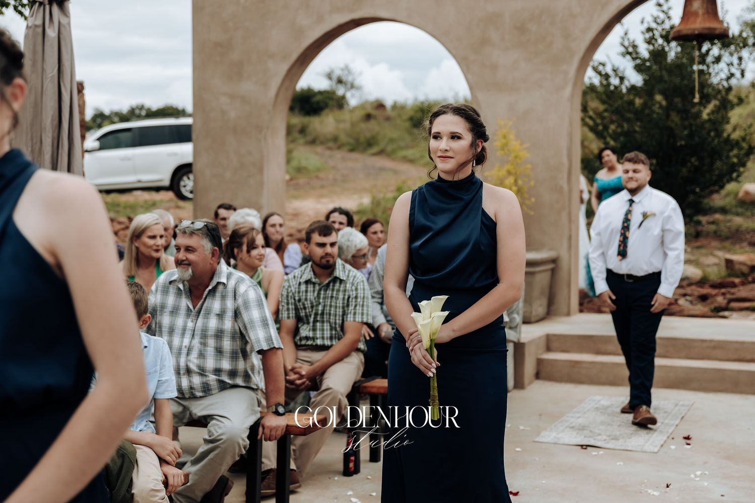 Outdoor wedding ceremony with guests seated under Mediterranean-style stone arches.