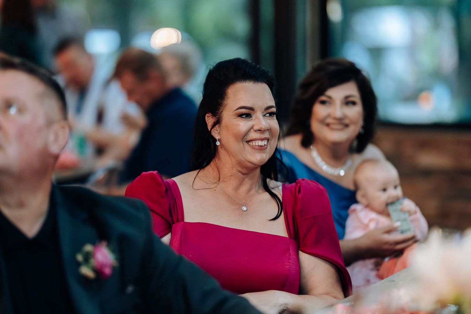 Wedding guests enjoy the reception celebration in a rustic indoor venue with warm lighting.