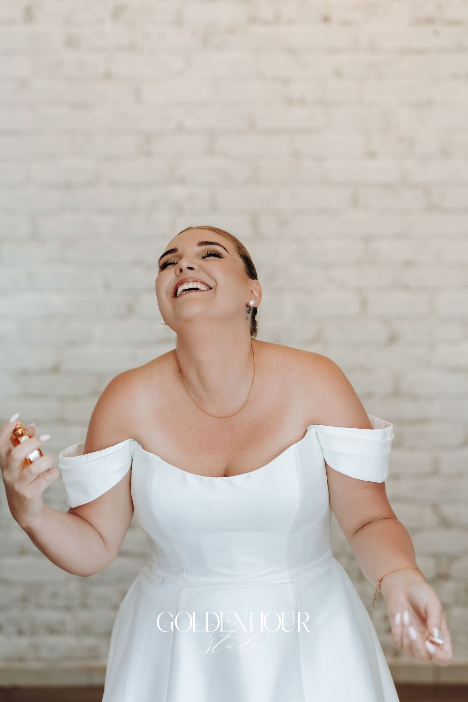 A bride in a white off-shoulder gown laughs joyfully during a candid wedding photo session.