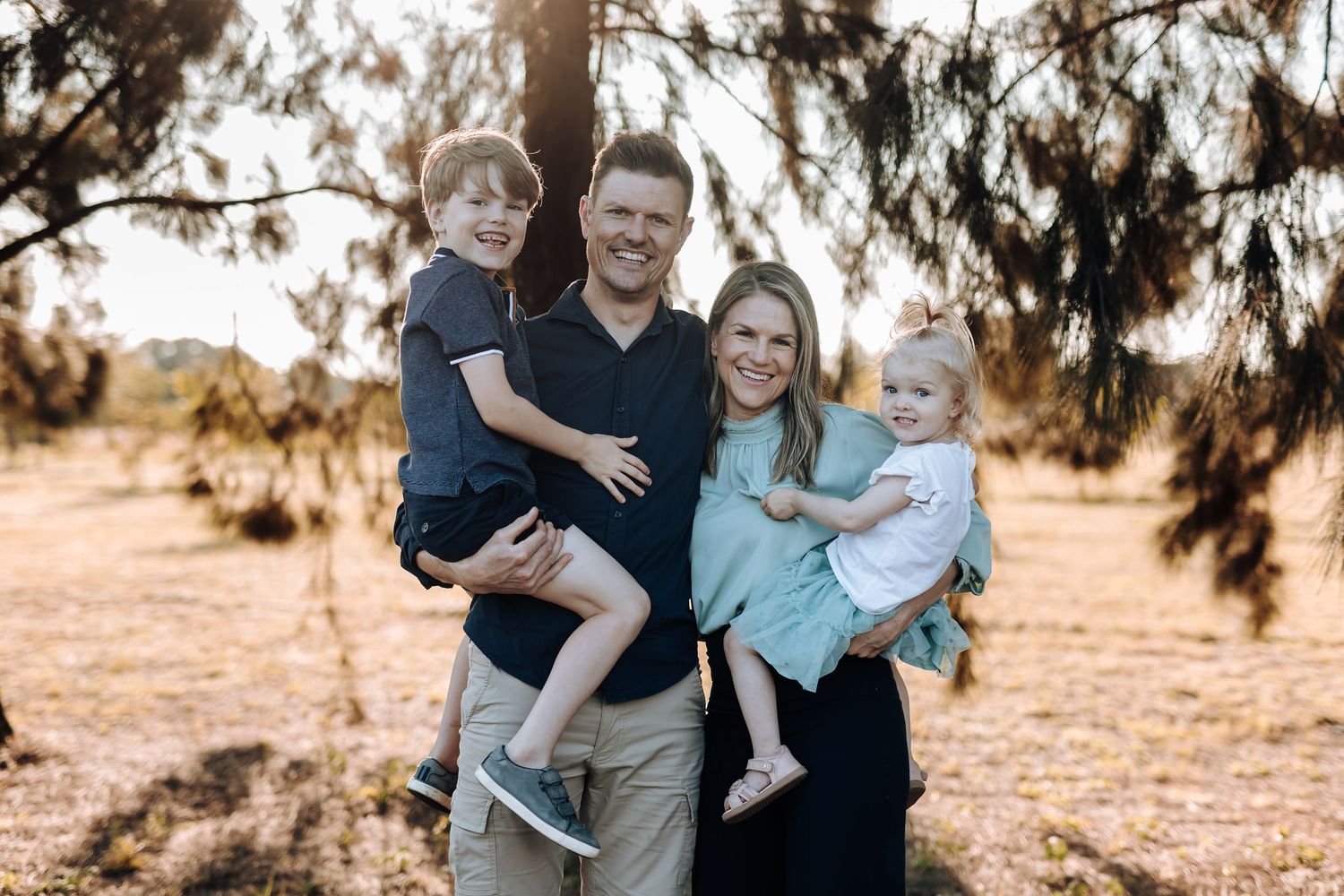 A group poses together outdoors at sunset in casual wear for an autumn family photoshoot.