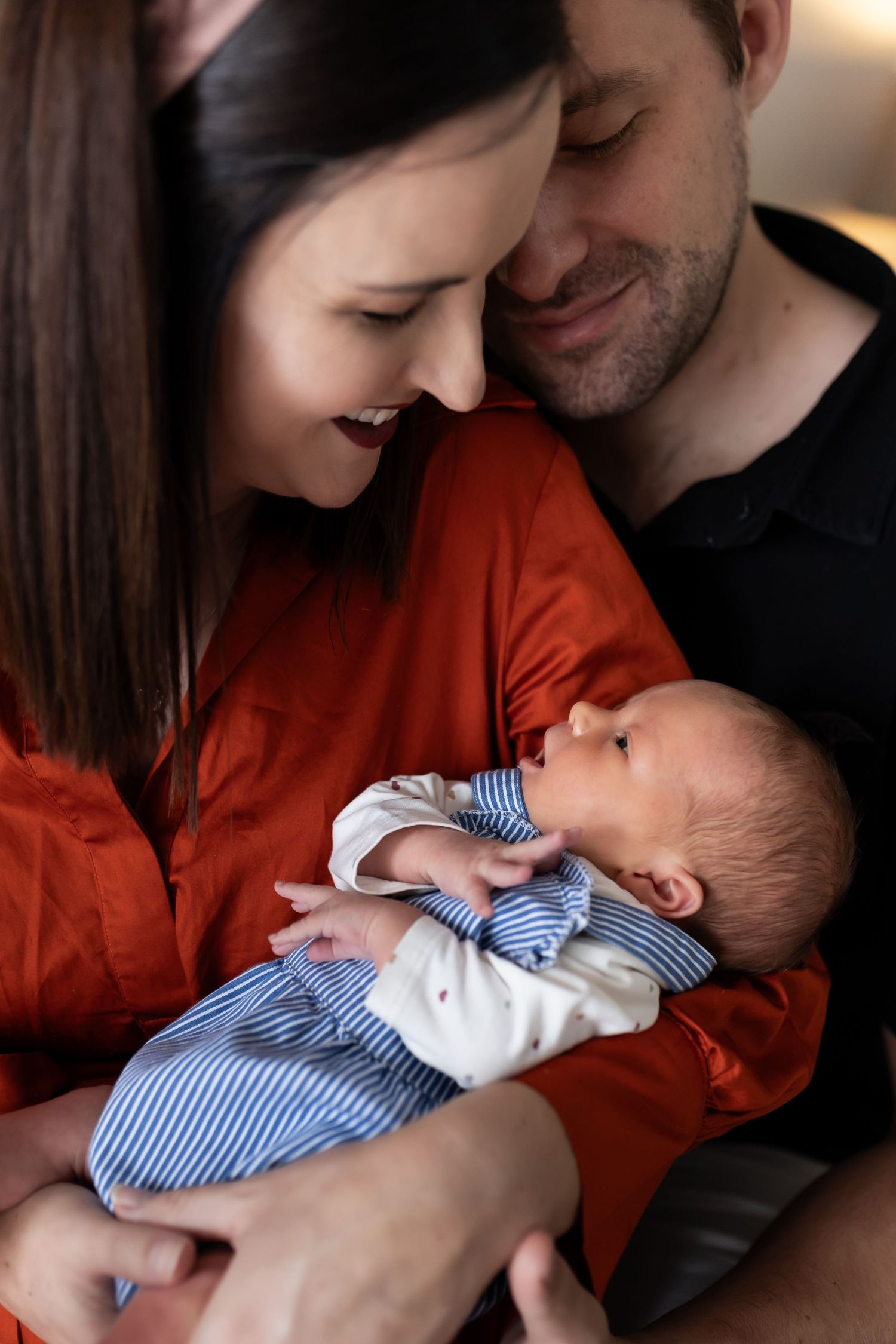Parents cradling infant in red and black clothing during an indoor family photo session.