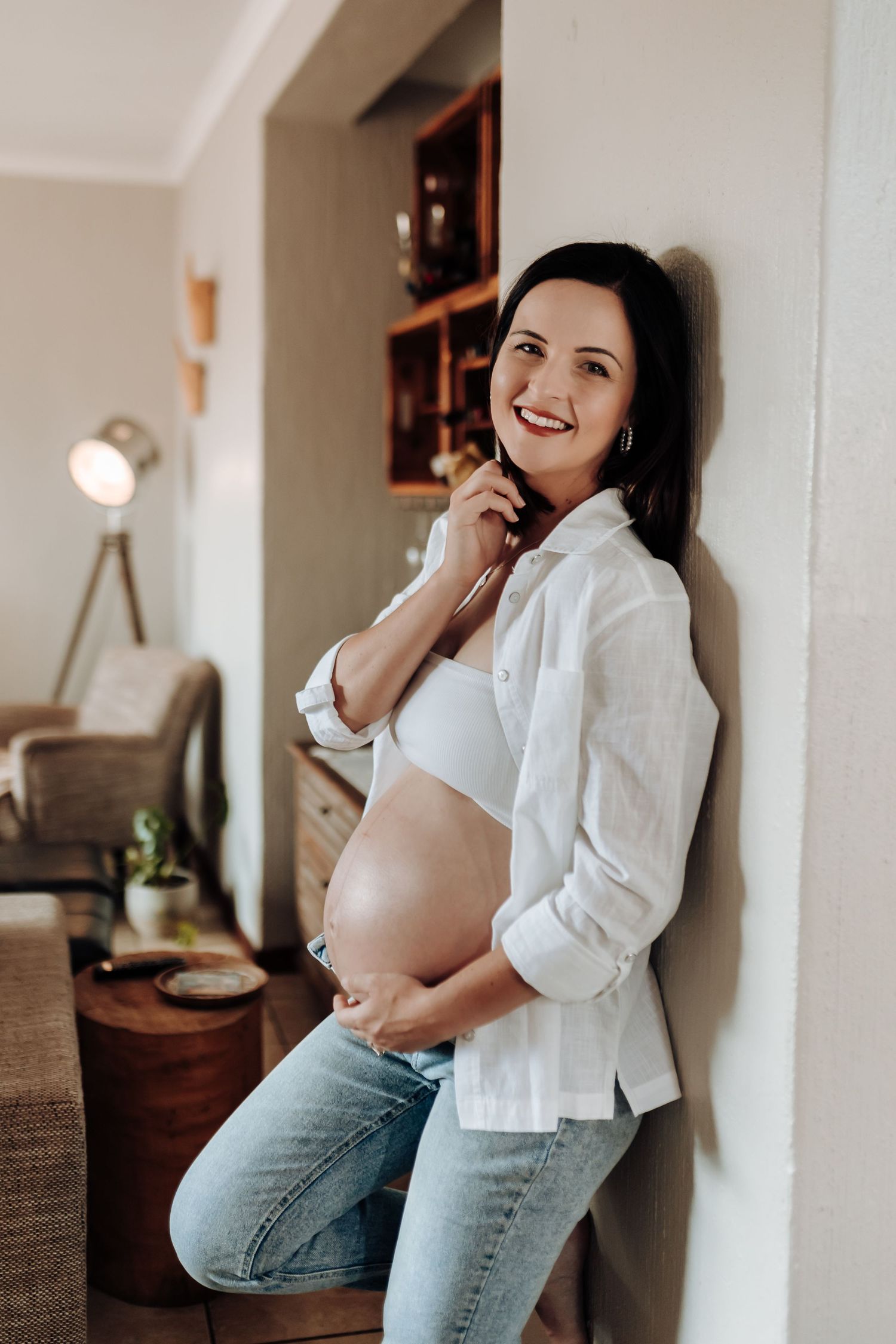 Series of intimate maternity photos showing someone in a white shirt and jeans posing against a wall in natural lighting.