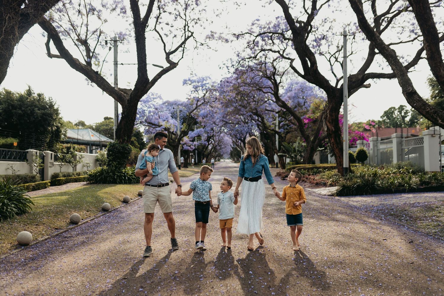 Group walking along a scenic street lined with blooming purple jacaranda trees on a sunny day.