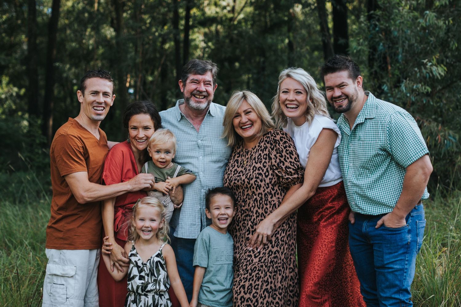 A joyful group poses together outdoors in a wooded setting on a sunny day.