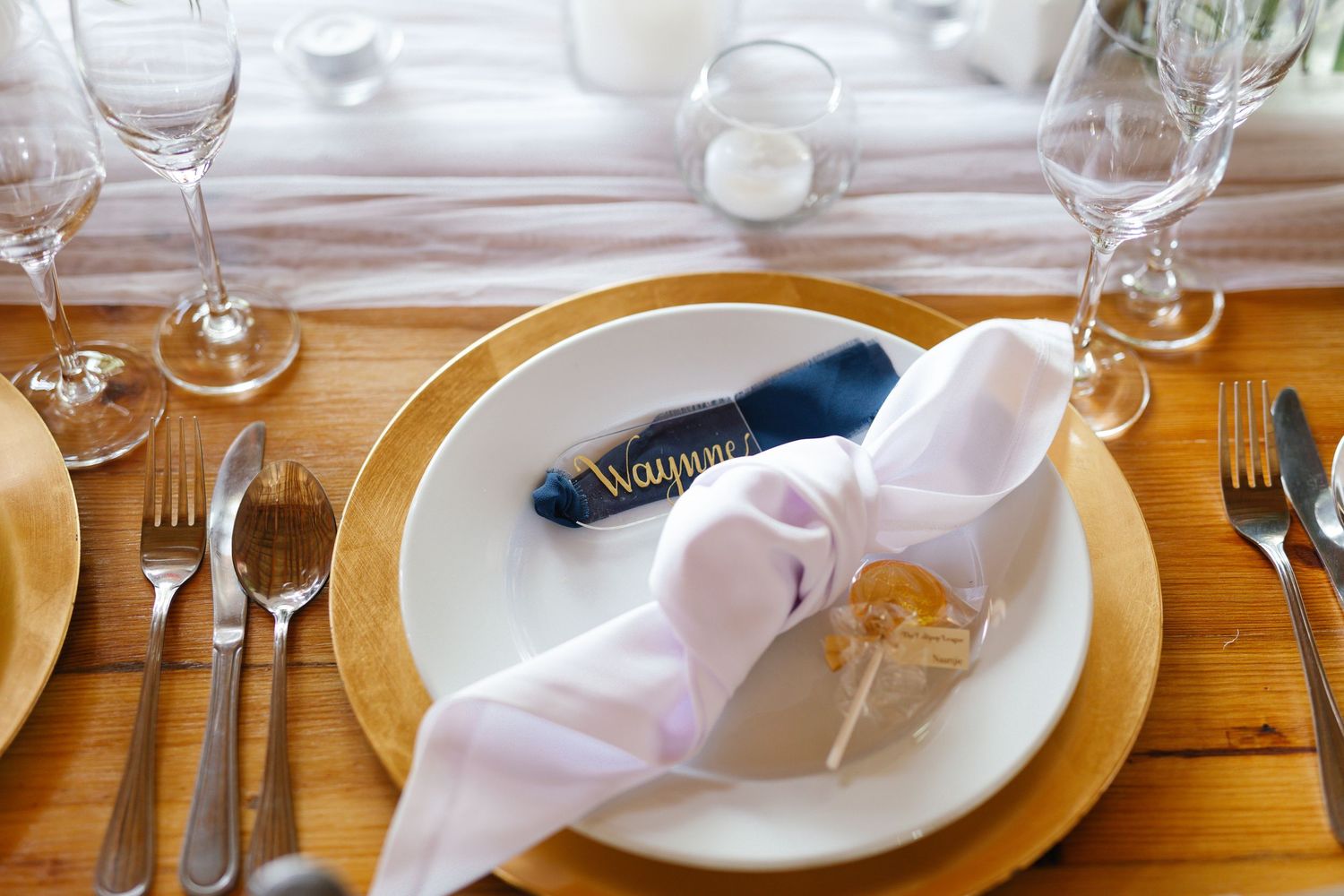 Elegant place settings with white plates, wine glasses, and silverware arranged on a rustic wooden table.