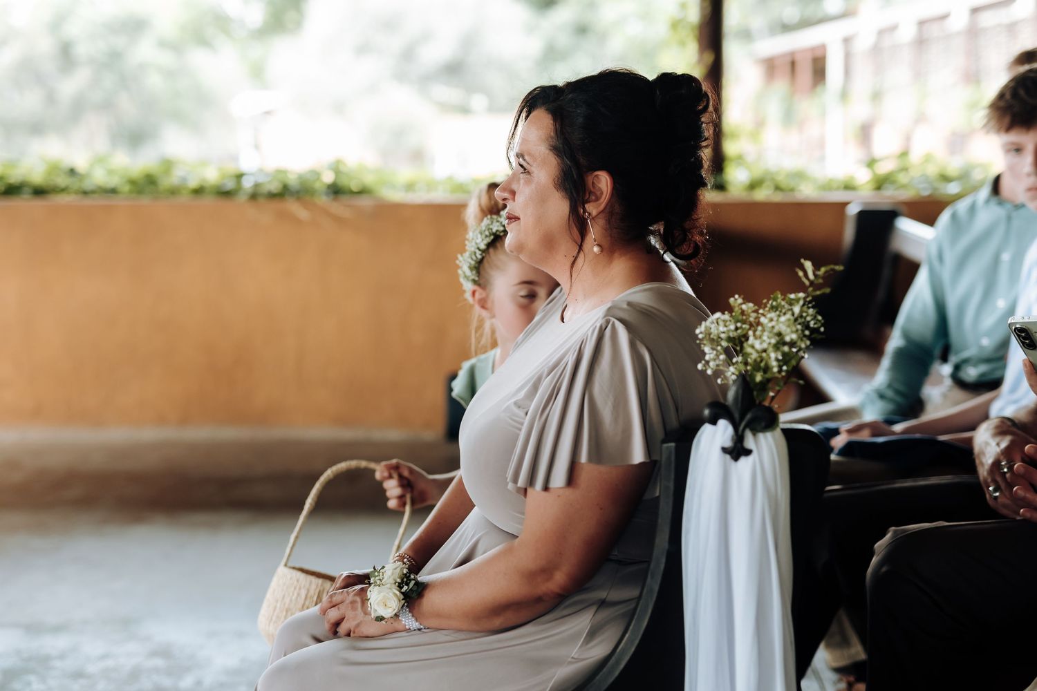 A wedding party sits at a long reception table decorated with greenery and floral centerpieces.