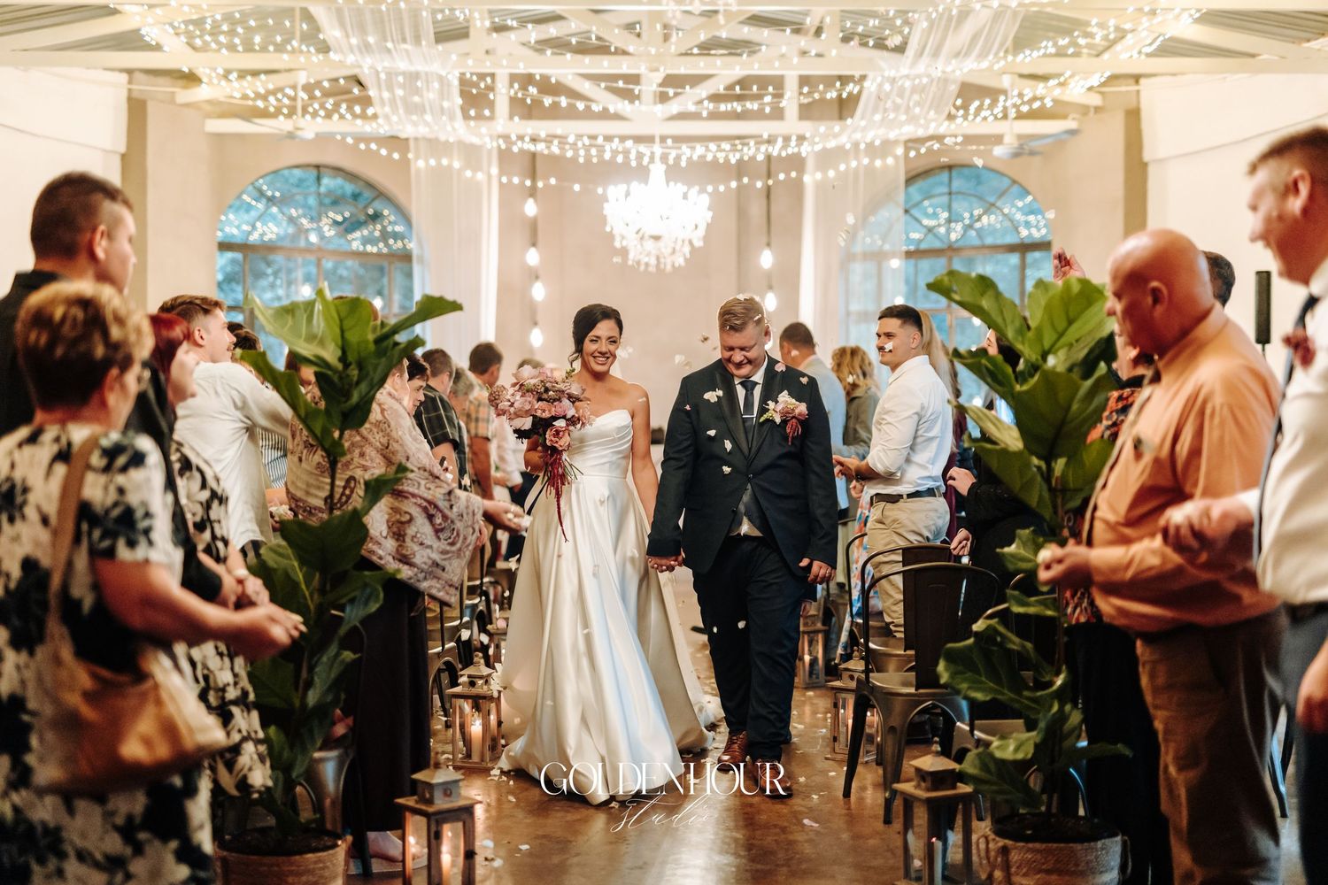 Newlyweds walking back down the aisle as guests celebrate with confetti in elegant venue.