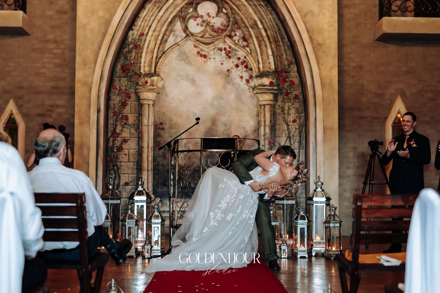 Bride and groom sharing first kiss at castle wedding altar with lanterns and floral arch decor.