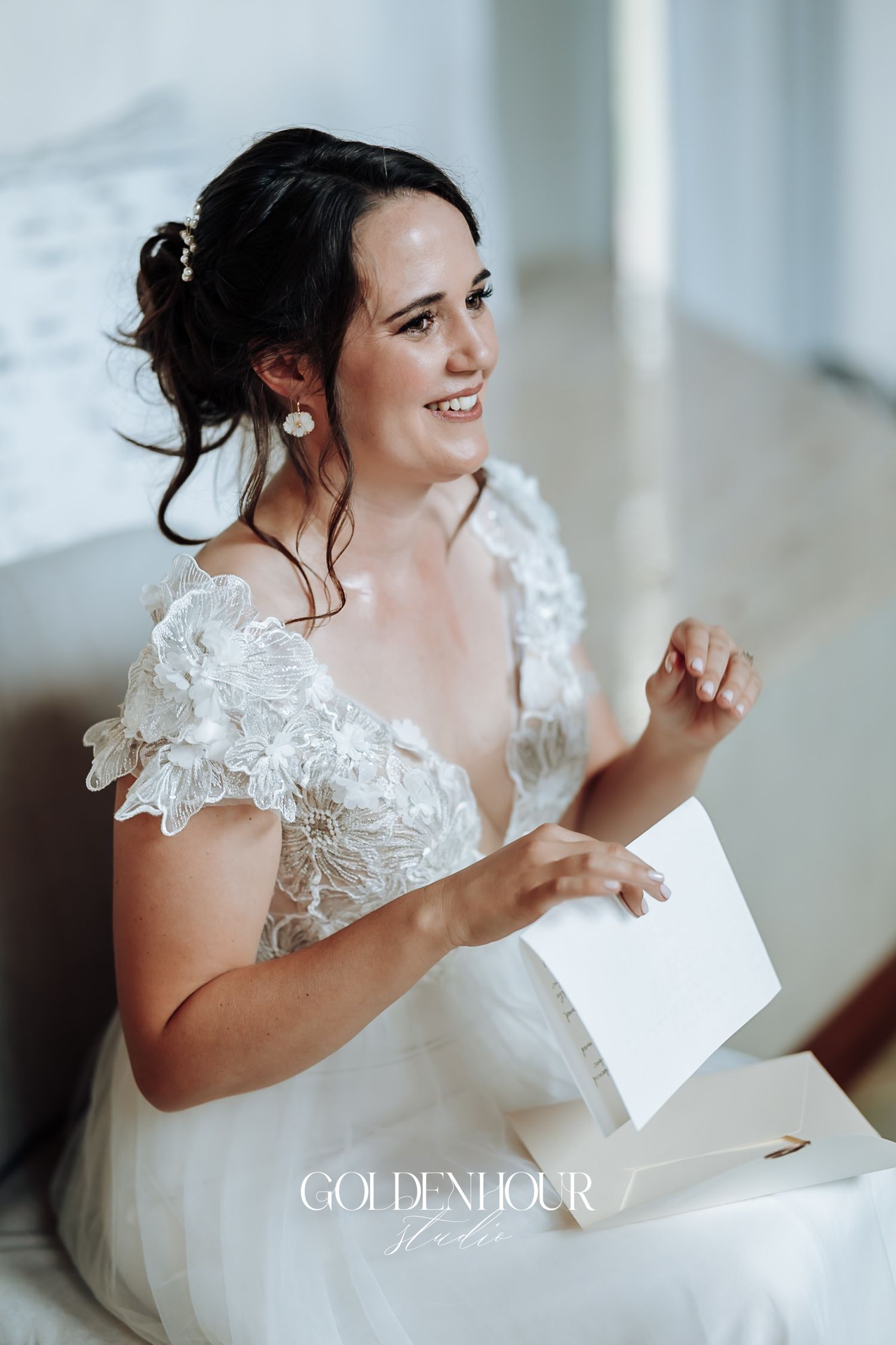 Radiant bride in off-shoulder lace wedding gown reading a heartfelt letter before the ceremony.