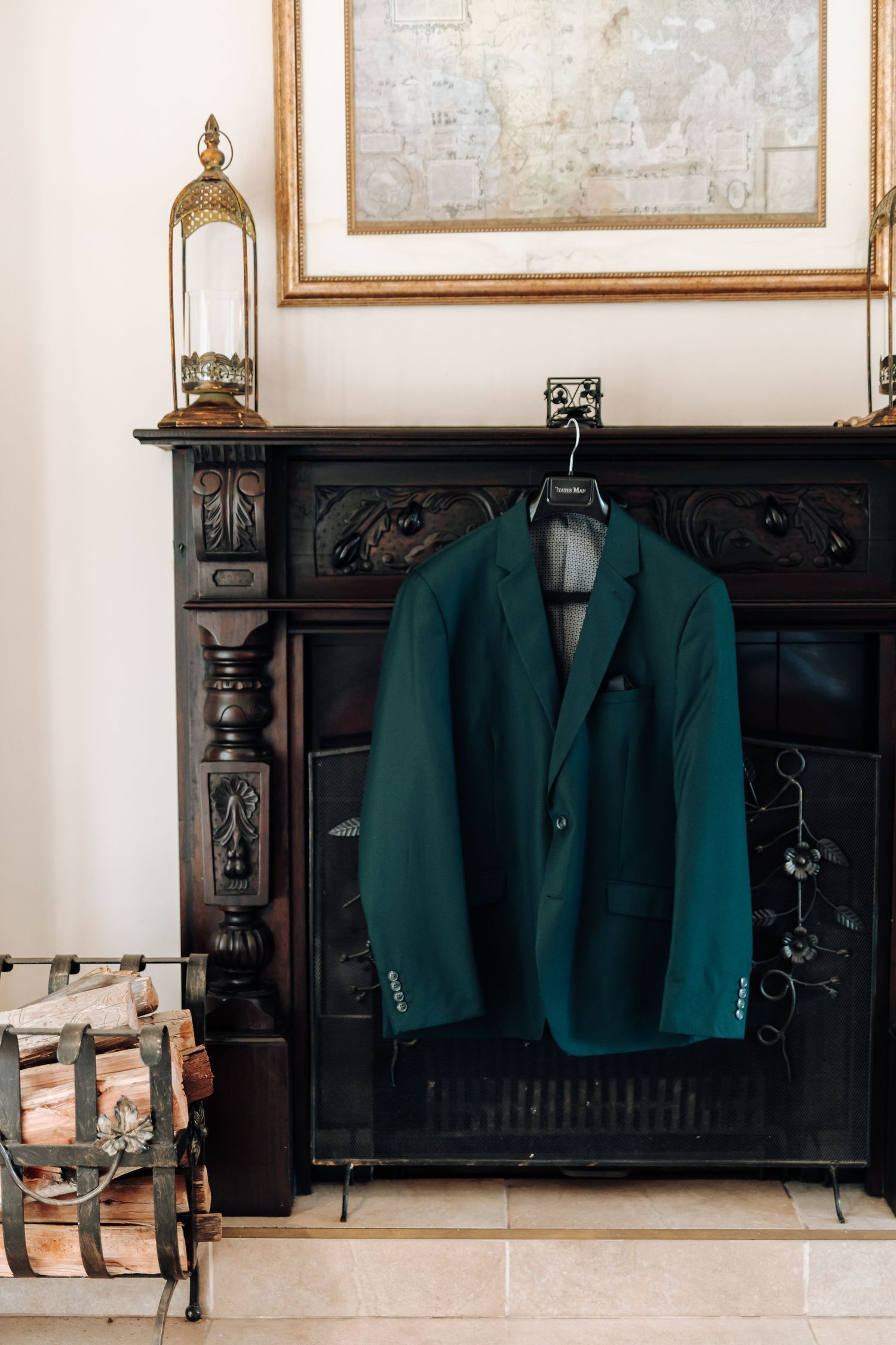 A dark green blazer hangs on a hanger against an ornate black fireplace mantel with vintage decor.