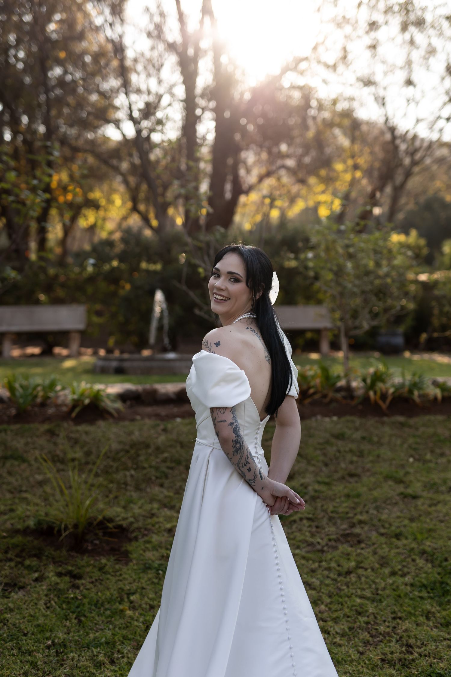 A bride in a classic white ball gown stands gracefully in a sunlit garden during golden hour.