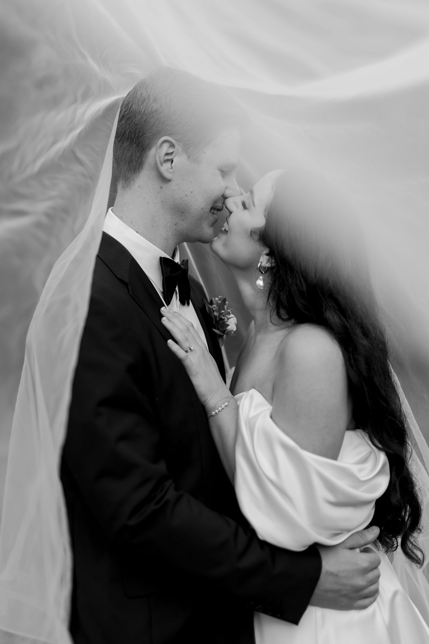 Artistic black and white wedding photo under flowing veil showing intimate moment.