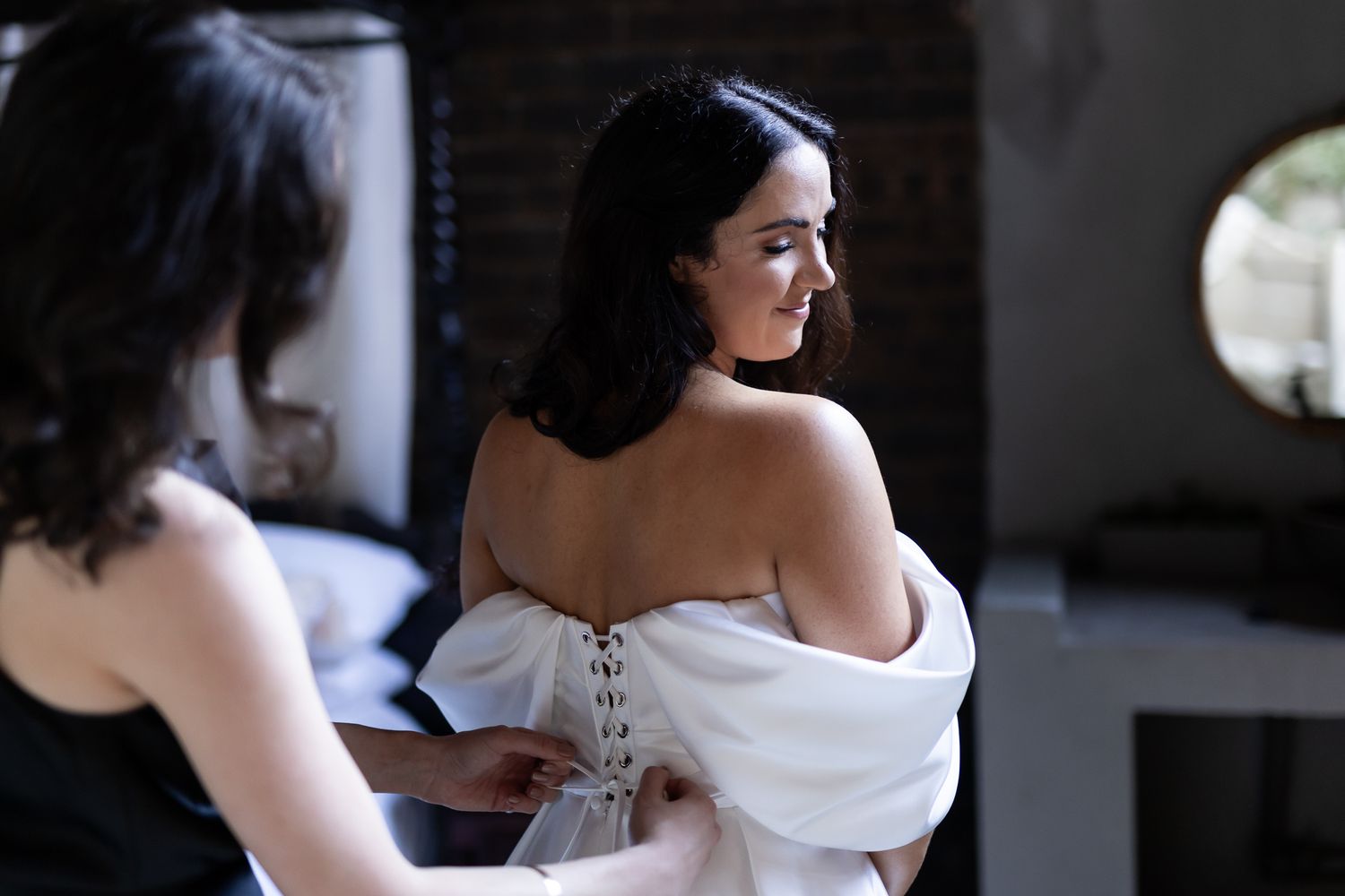Intimate getting ready moment as wedding dress is secured in natural window light.