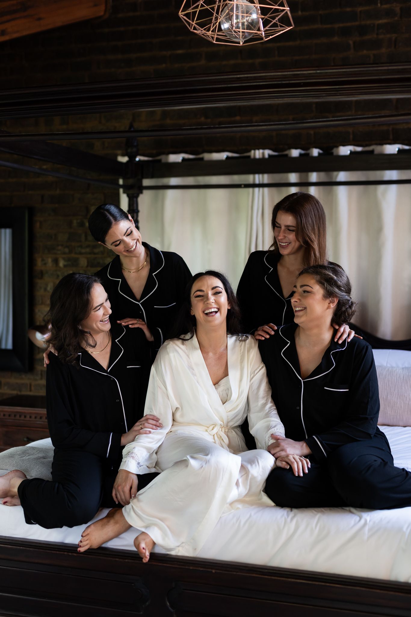 Bridal party in matching pajamas share joyful moment on bed in rustic room.