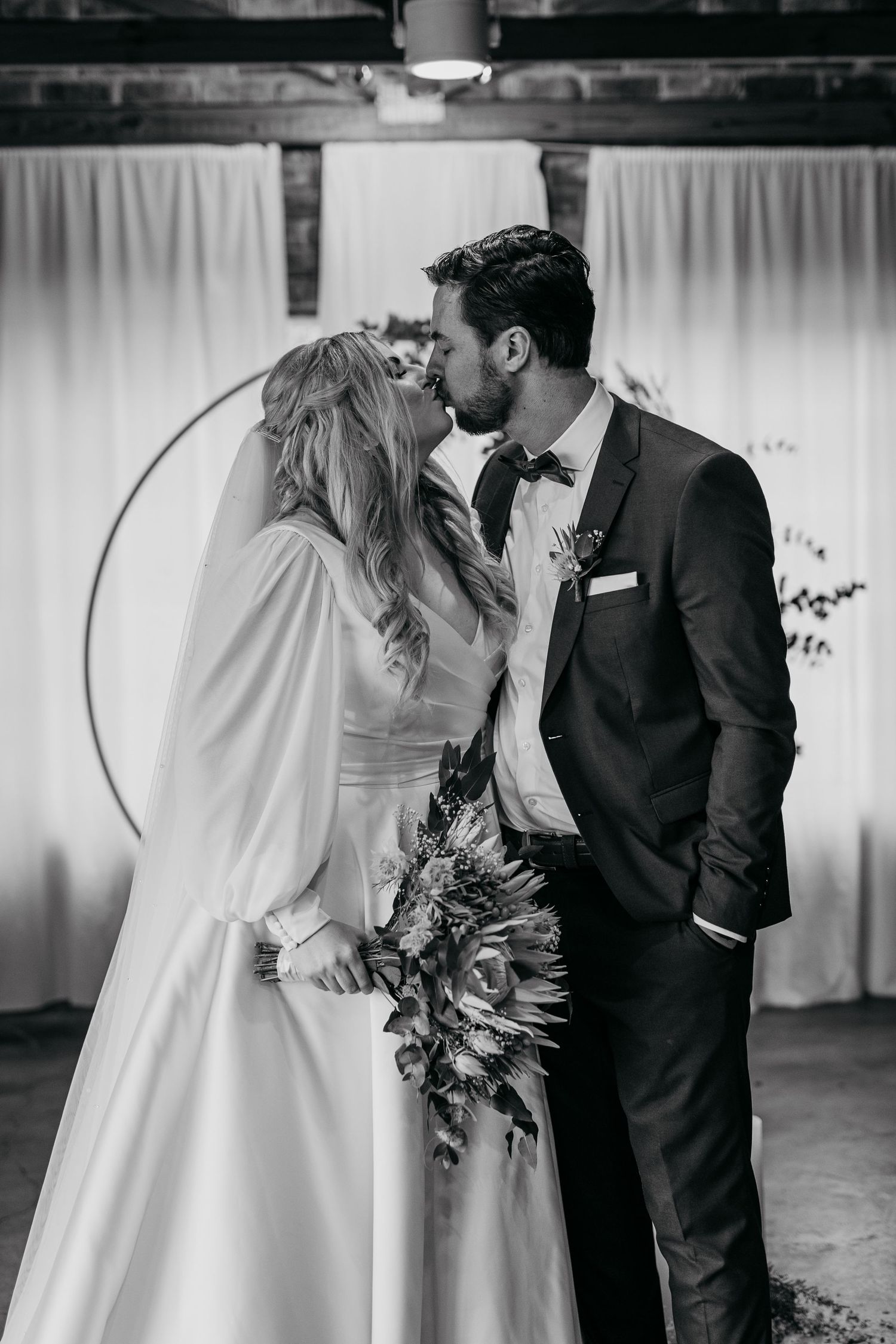 Black and white portrait of newlyweds sharing an intimate moment against white draping backdrop.