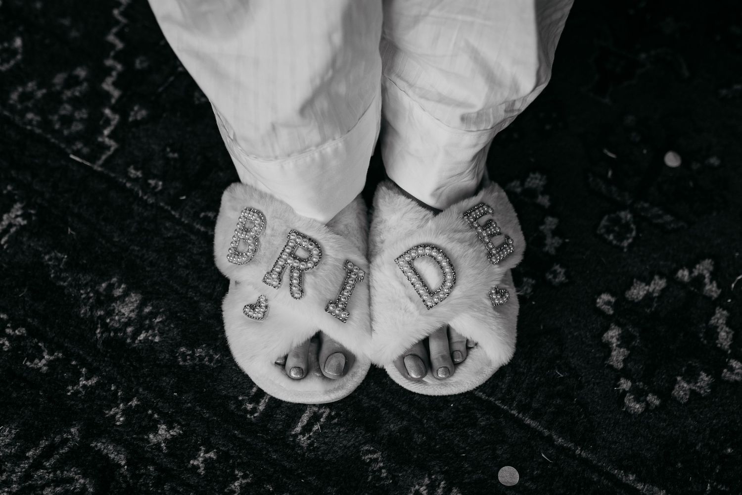 White slippers with 'BRIDE' written on them shown on dark flooring.