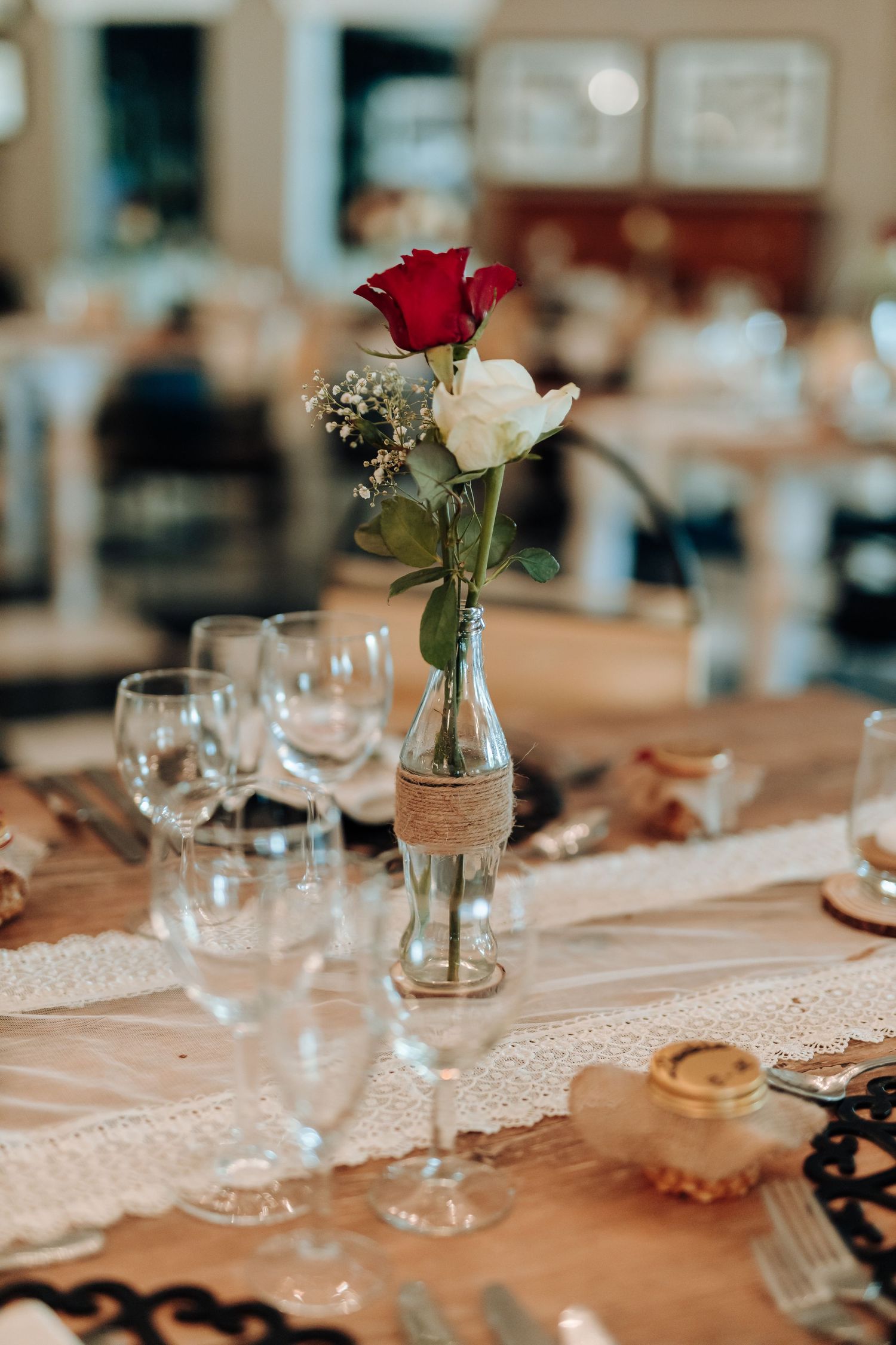 Close-up of wedding table setting with red and white roses in twine-wrapped glass vase.