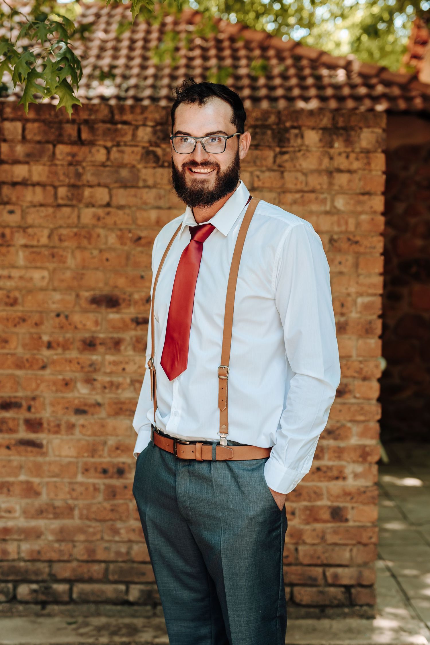 Business casual outfit with suspenders and red tie against rustic brick background.