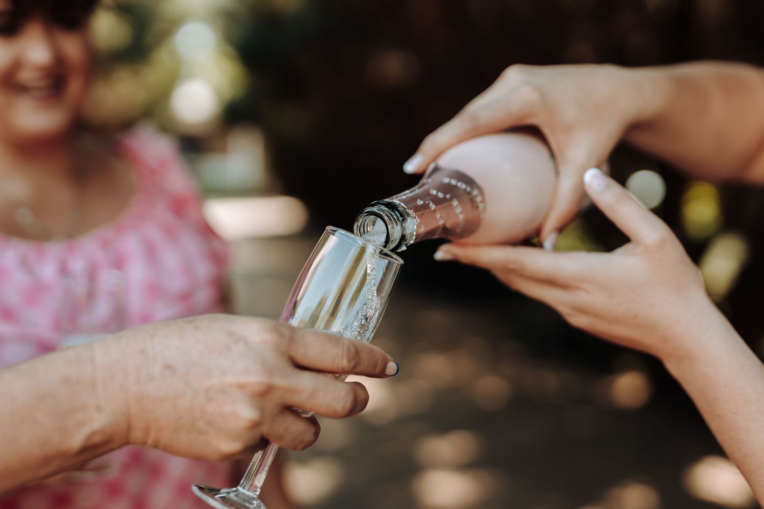 Hands pouring champagne into glass during outdoor celebration.