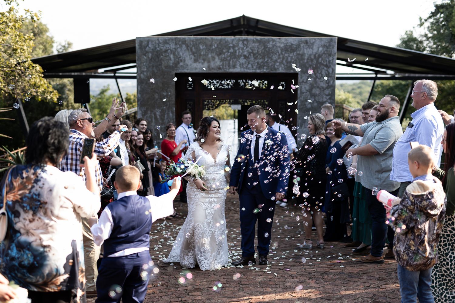Wedding guests throw confetti as newlyweds exit outdoor ceremony venue.