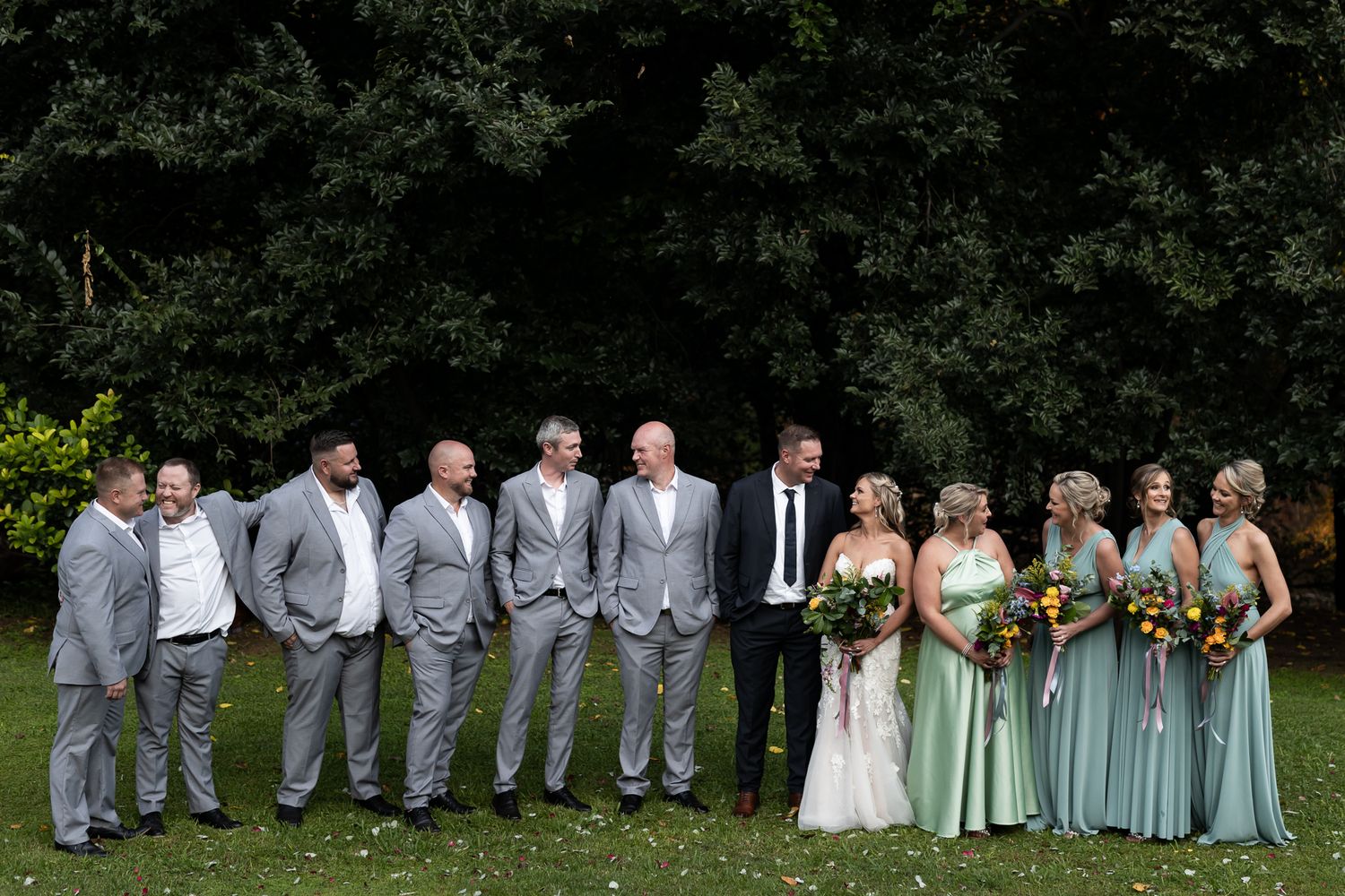Wedding party in grey suits and mint green dresses posed together outdoors.