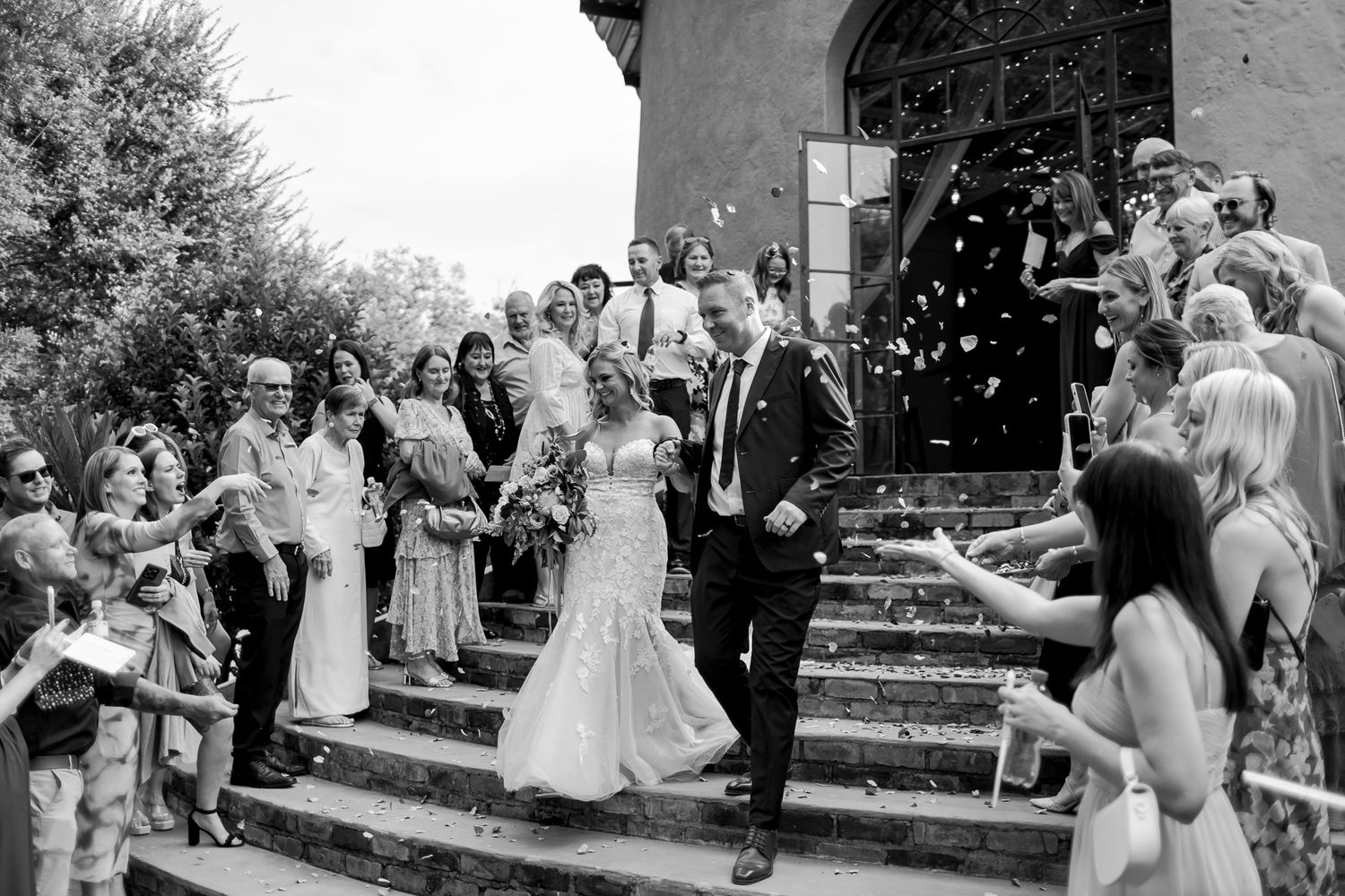 Black and white photo of wedding party exiting church while guests throw confetti in celebration.