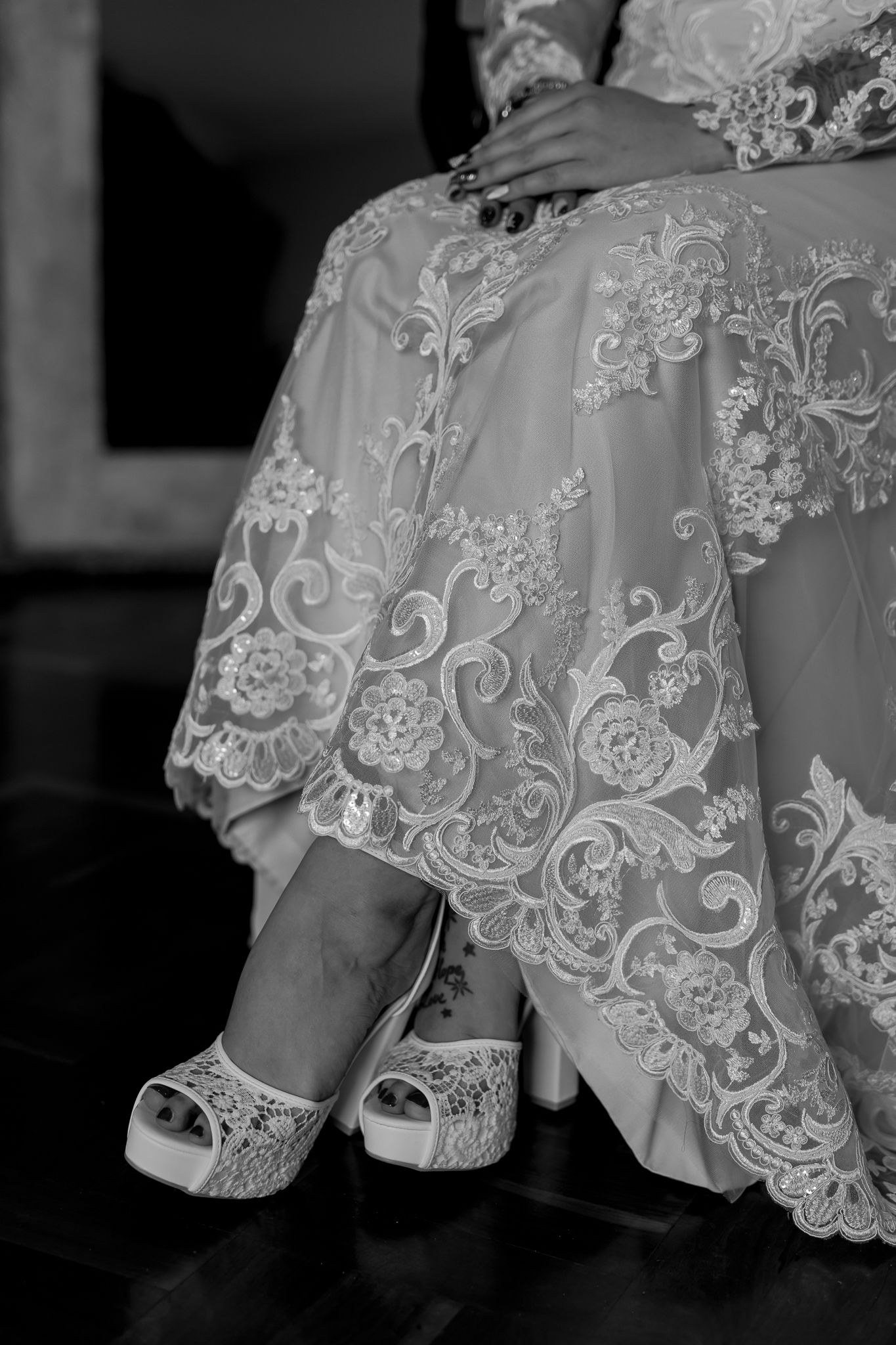 Close-up of intricate lace wedding dress hem and white peep-toe platform bridal shoes.