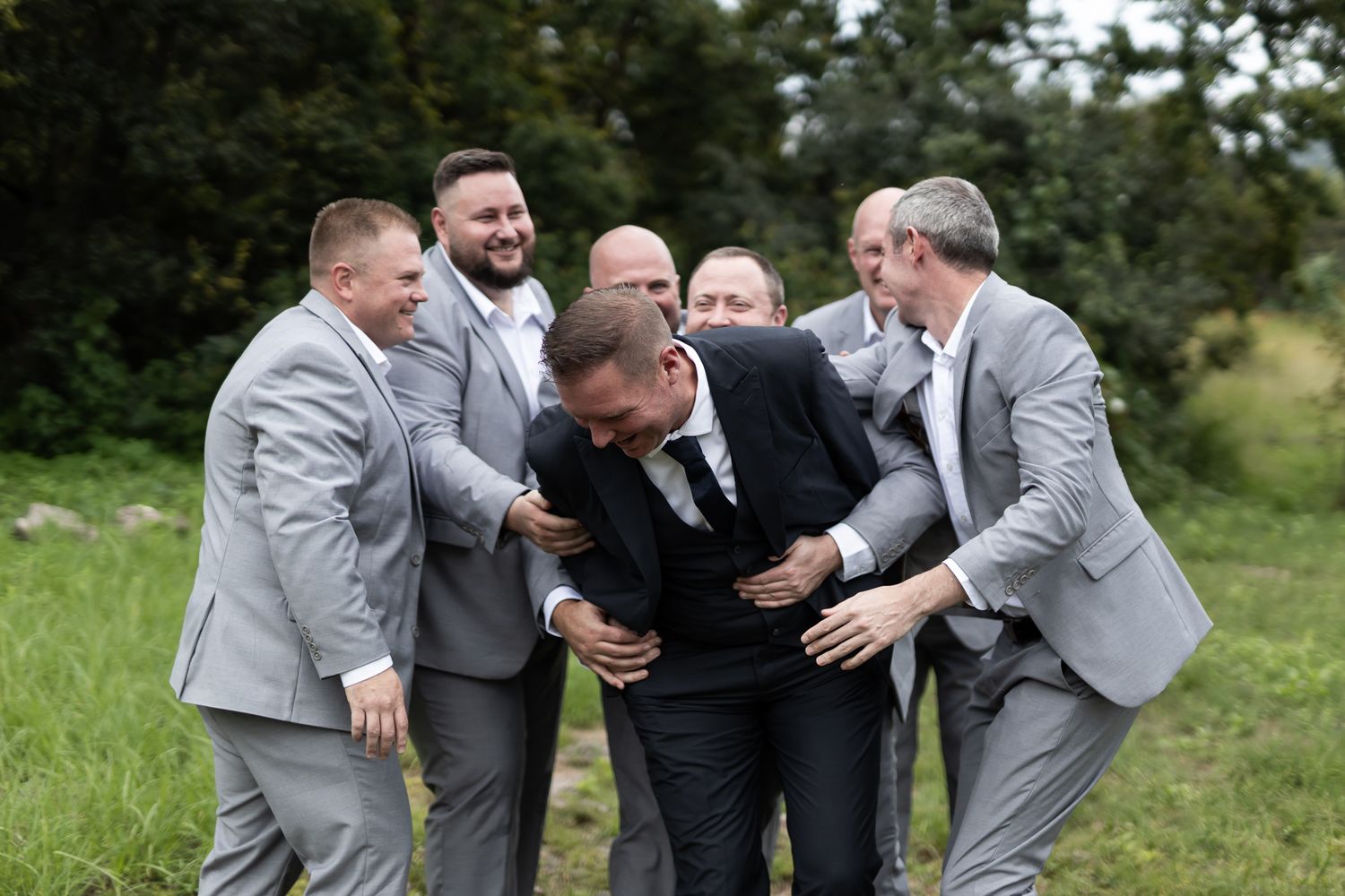 Groomsmen in gray suits laughing and joking with the groom in black.