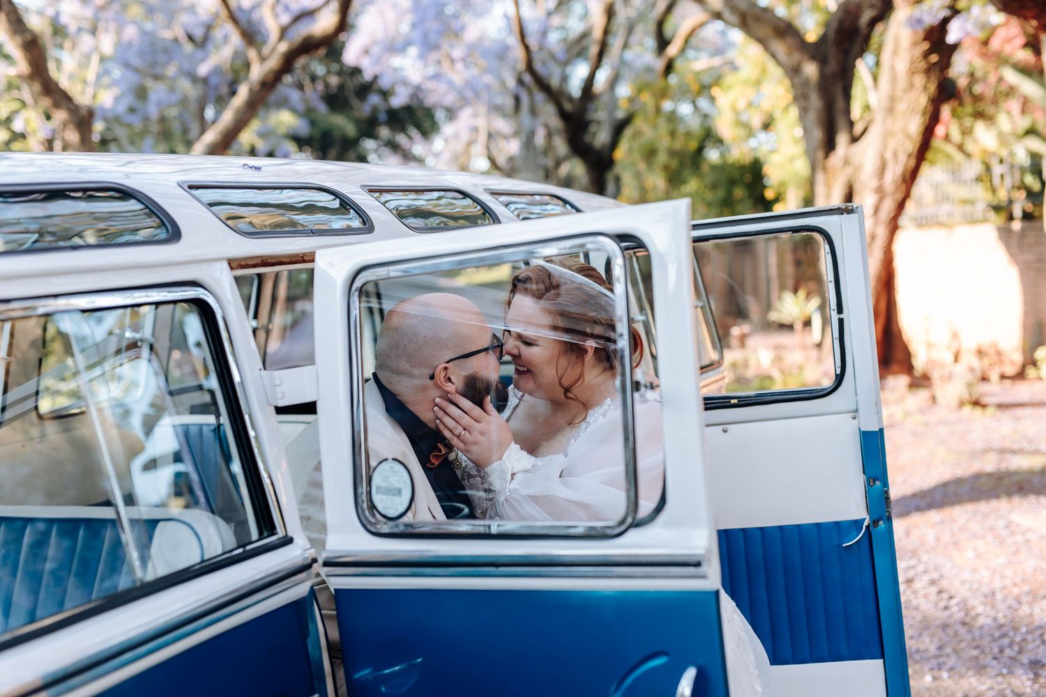 A classic blue and white vintage Volkswagen van parked in a sunny outdoor setting with trees in the background.