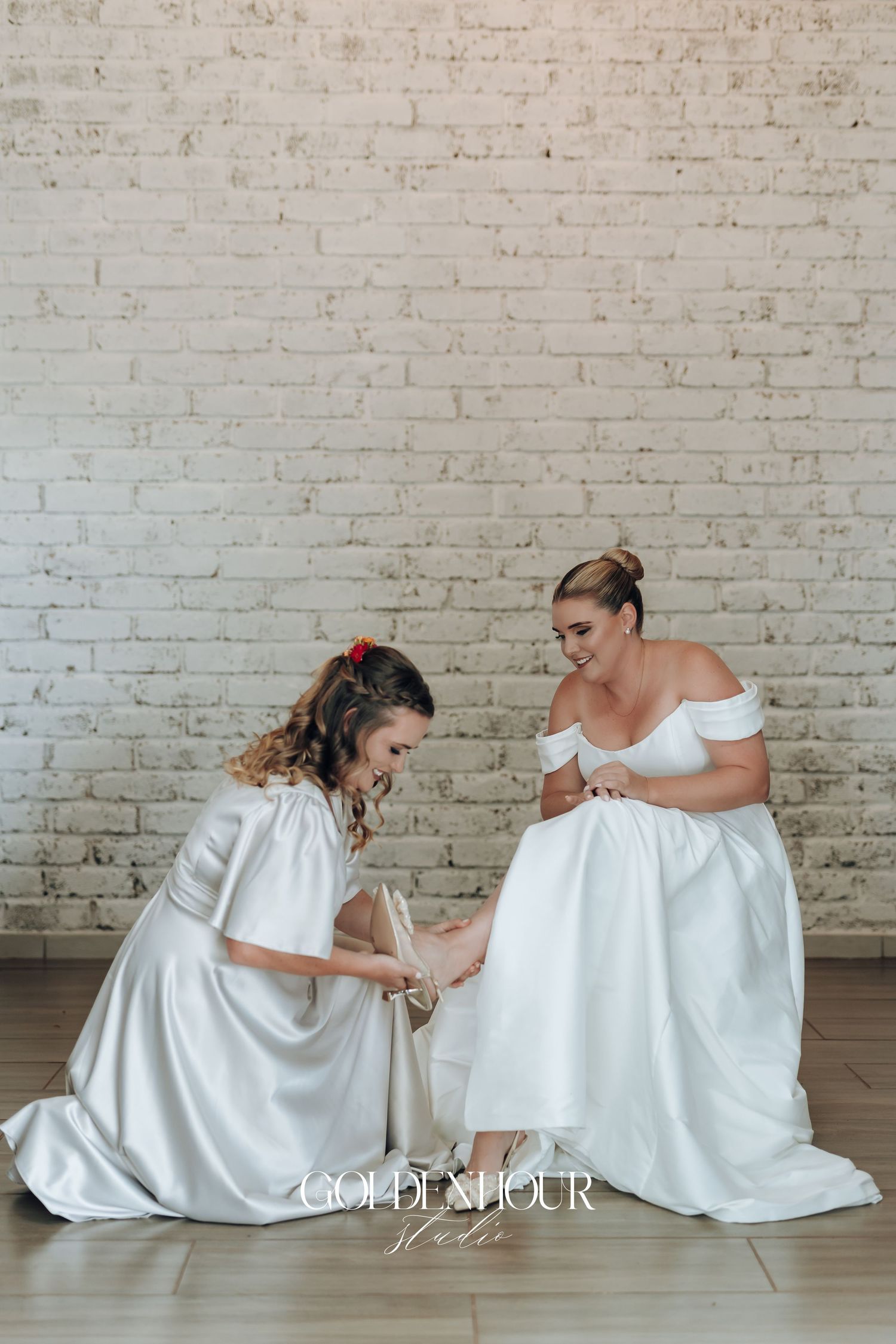 Two people in white dresses share tender moments in a sequence of photos against a brick wall background.