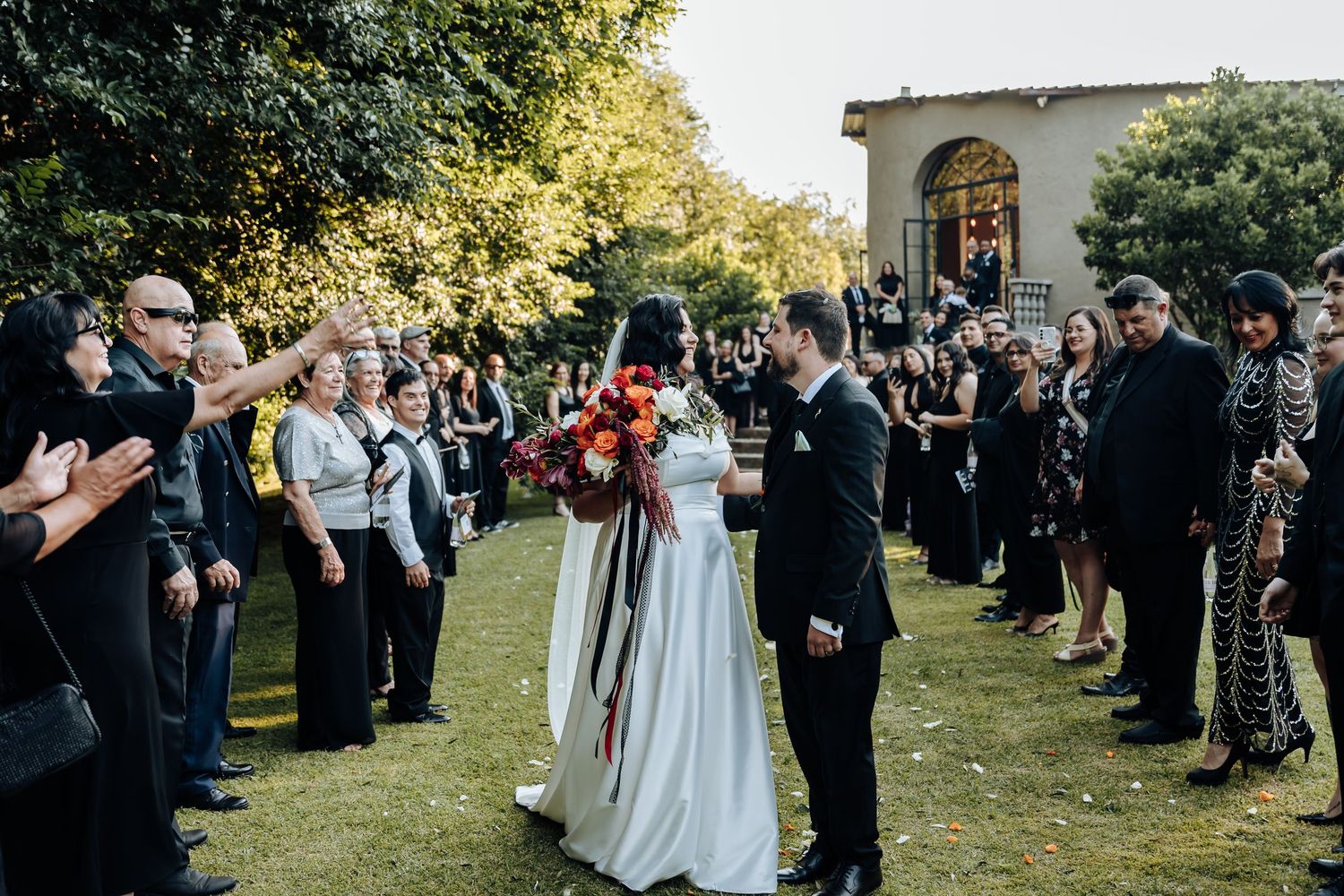 Wedding guests line up outdoors to celebrate the newlyweds on a sunny autumn day.
